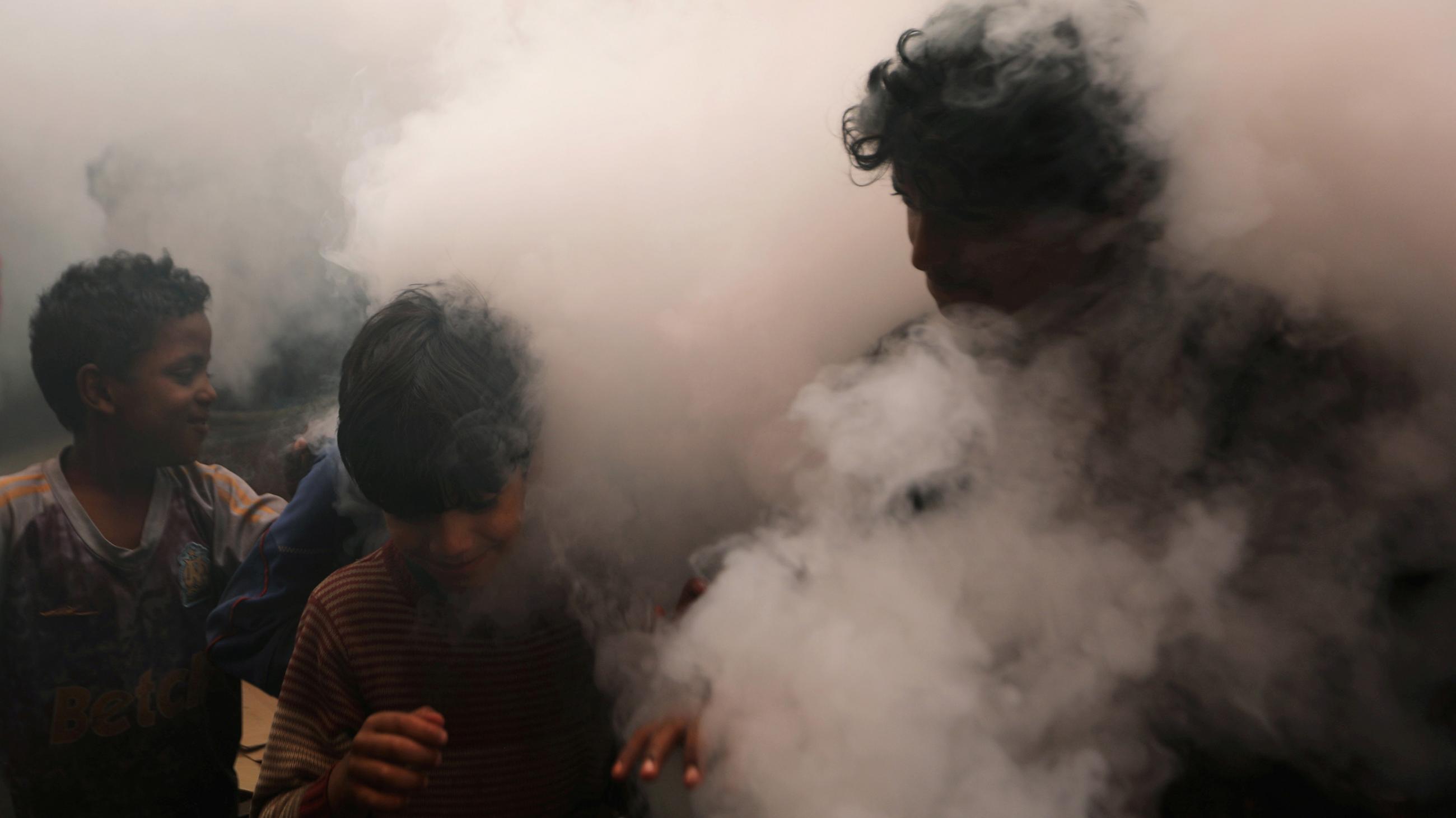 This is a powerful photo showing one man and two boys walking through a thick cloud of disinfectant mist.