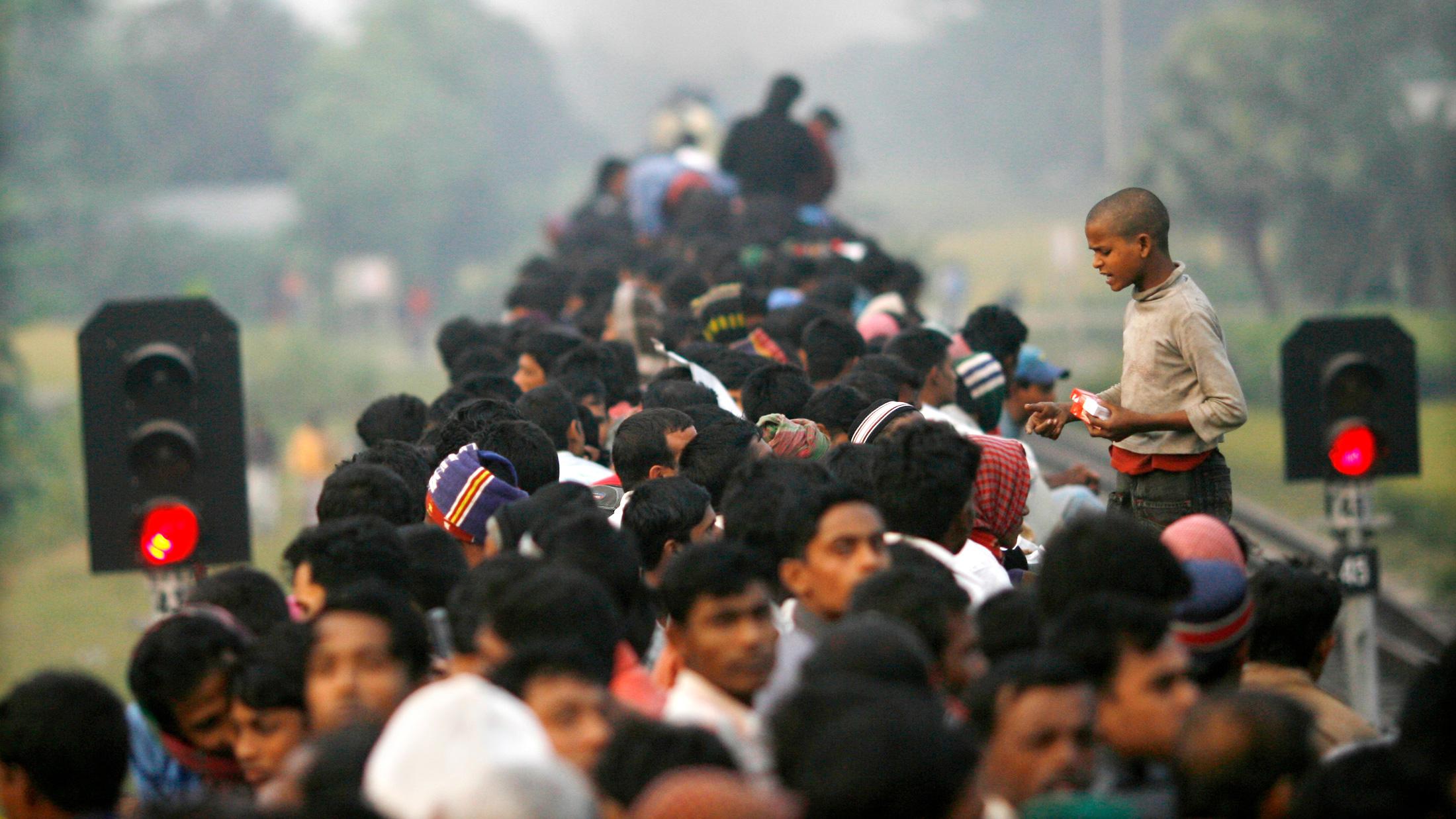 The photo shows a boy standing above a crowd of seated adults hawking smokes. 