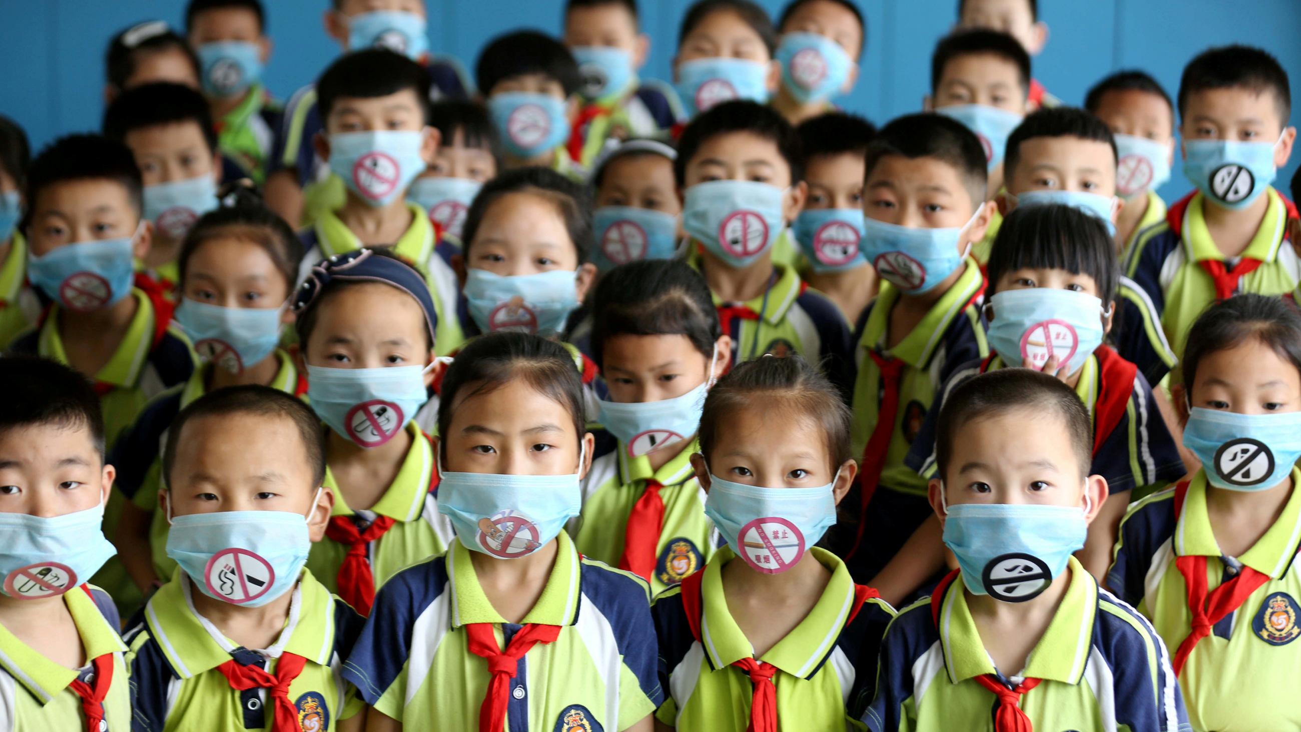 The photo shows a room full of children in school uniforms and no-smoking masks.