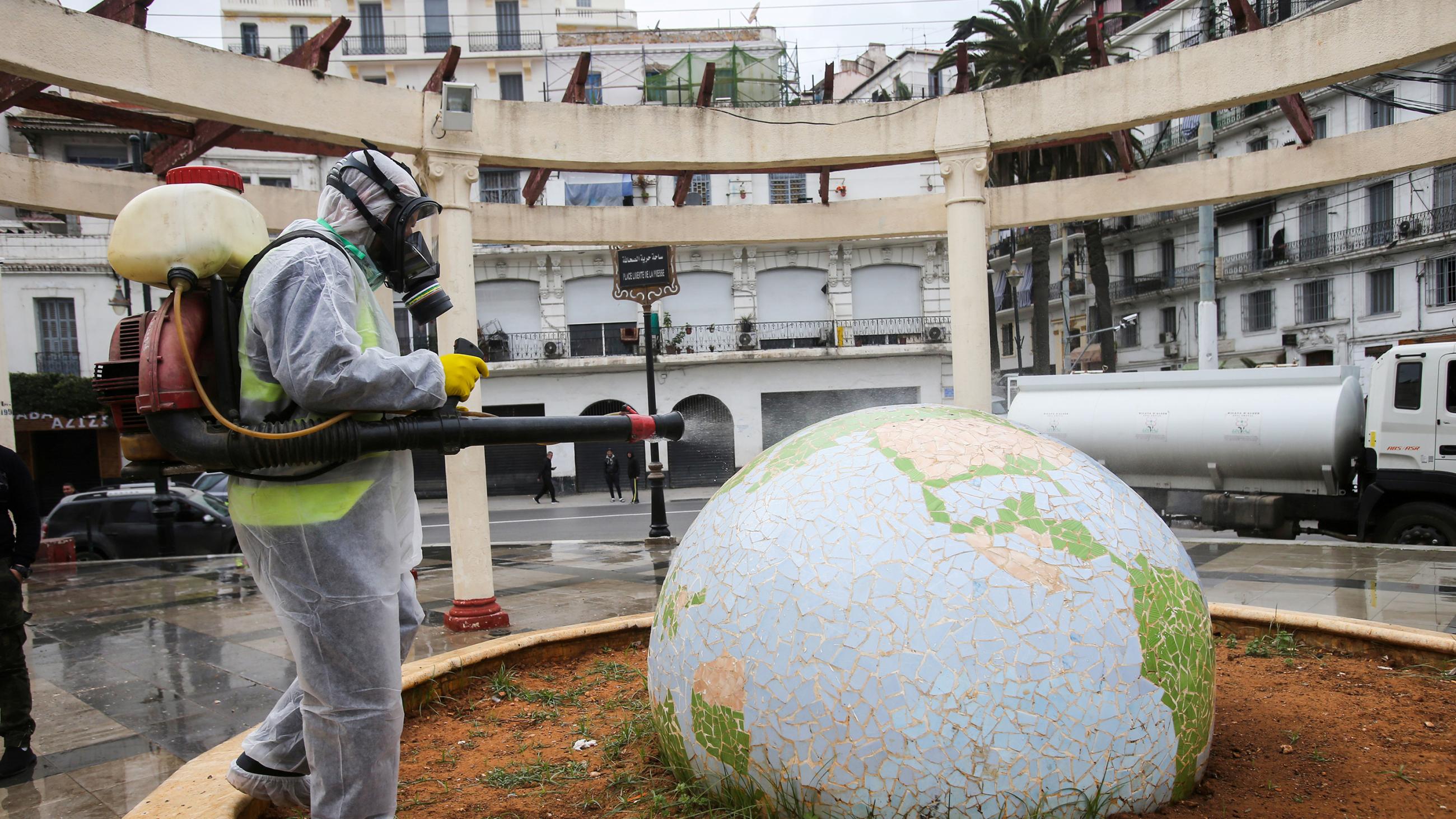 This is a bizarre photo showing the worker in a protective space suit spraying a large, fancy globe sculpture in the center of an open-air atrium. 