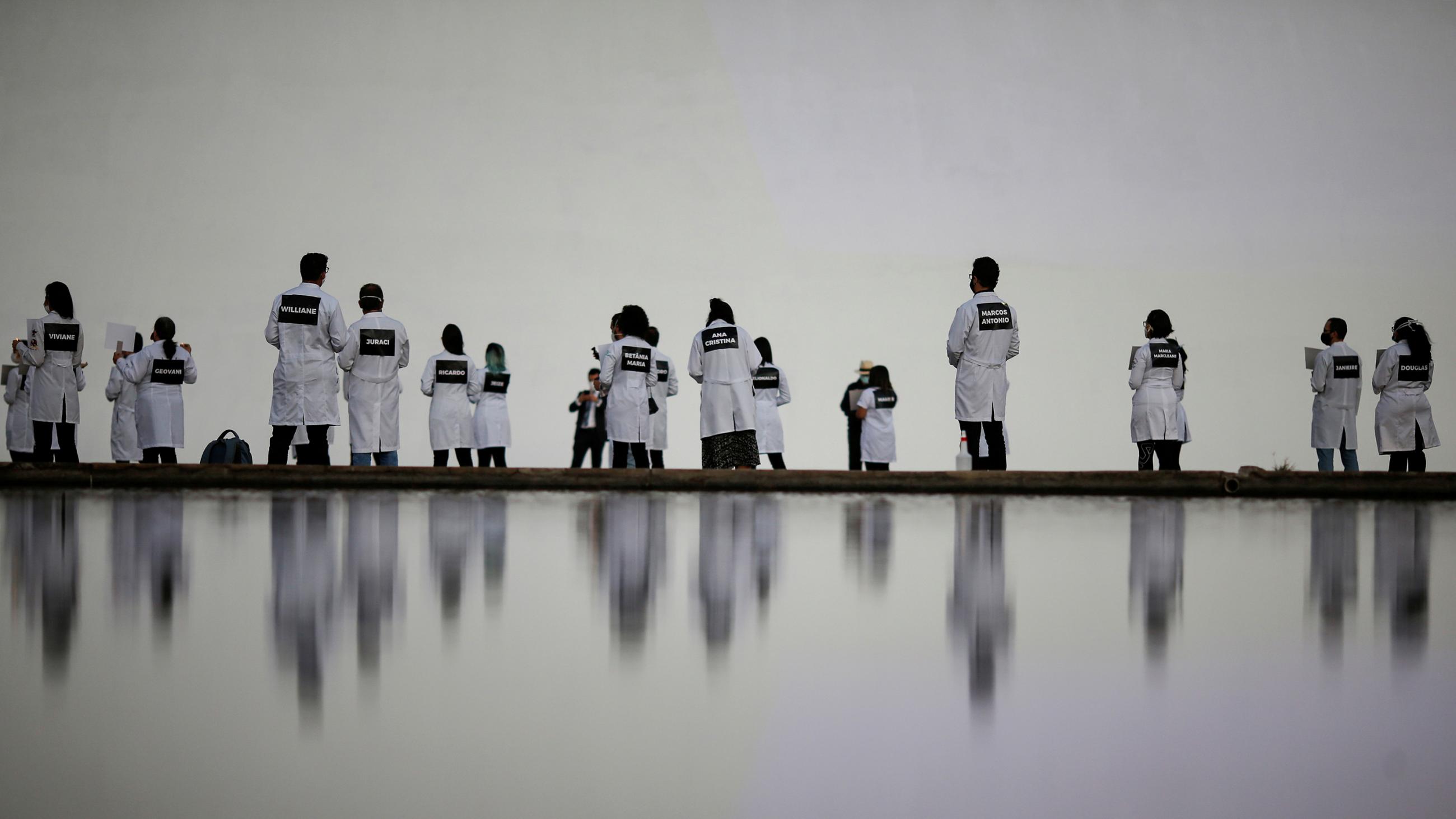 The image showsa bunch of people wearing white nurses' uniforms standing in the distance by a reflecting pool. 