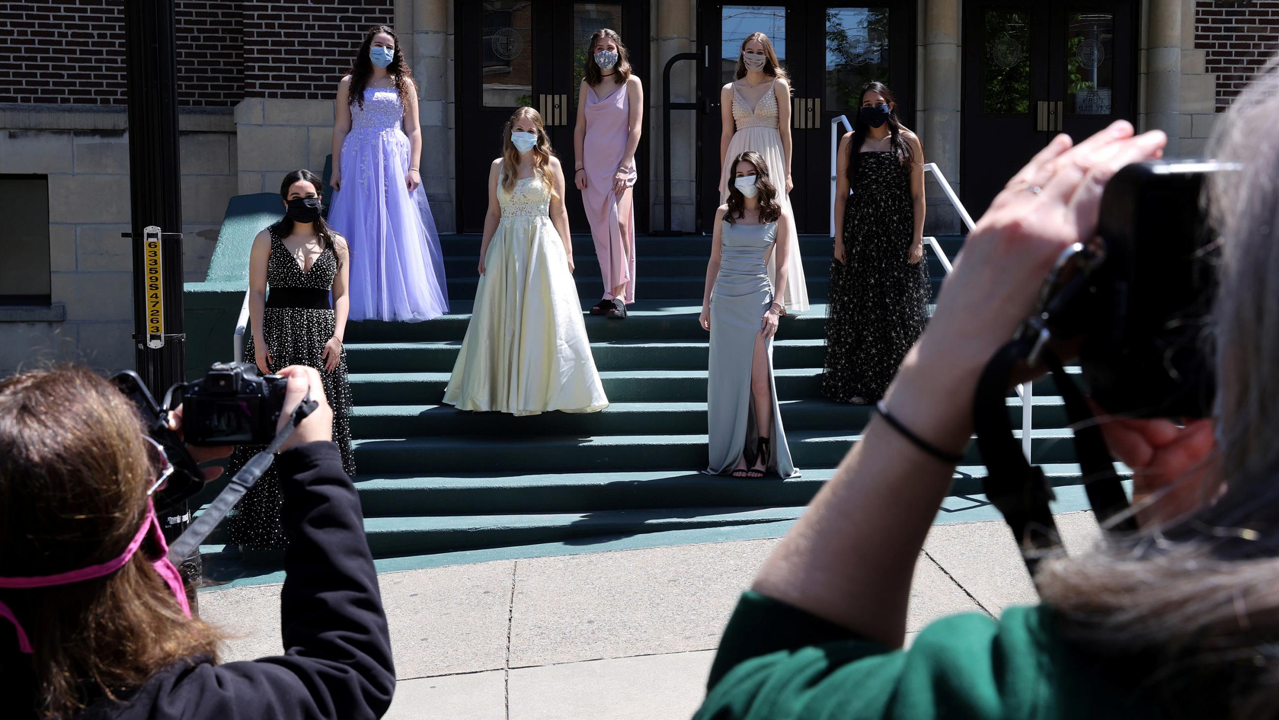 The photo shows several young women in Prom dresses posing on some steps while others (presumably their parents) take photos. 