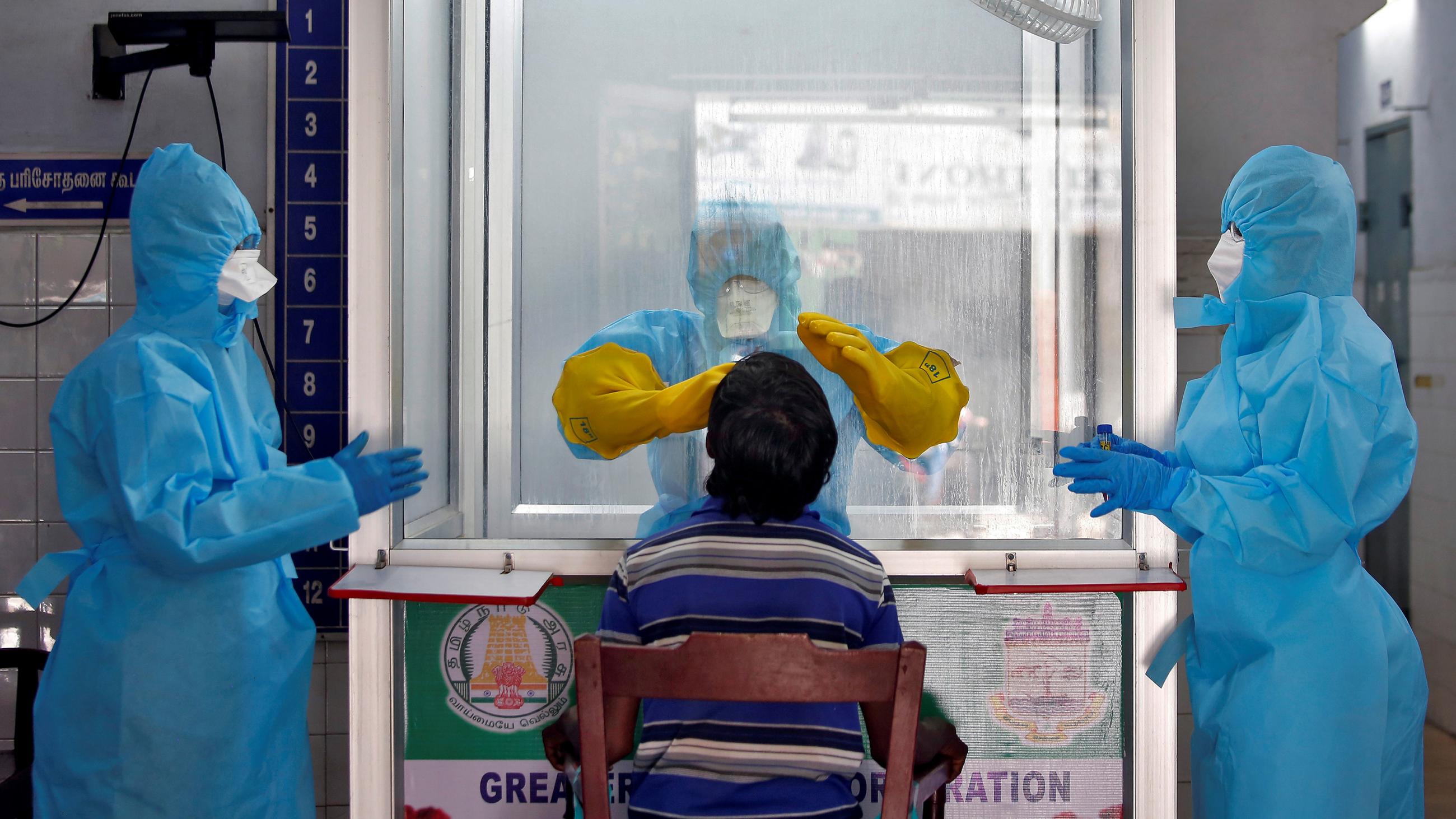 This is an amazing image with a man inside a booth that has holes and gloves for their hands administering to a prospective patient with two other health workers in protective gear standing on either side. 