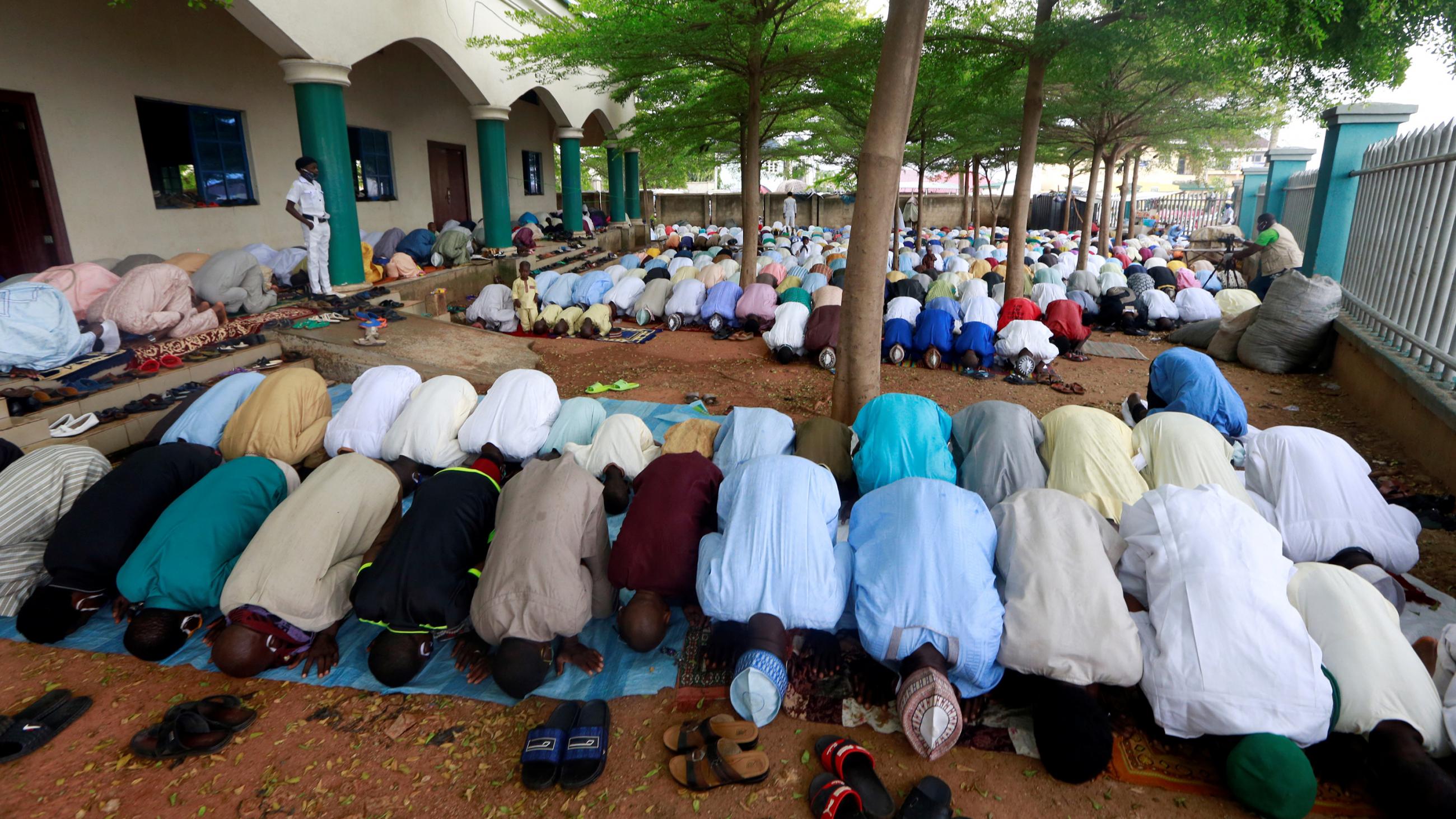 The photo shows a large gathering of people in an outdoor area praying, on their knees and prostrate on the ground. 