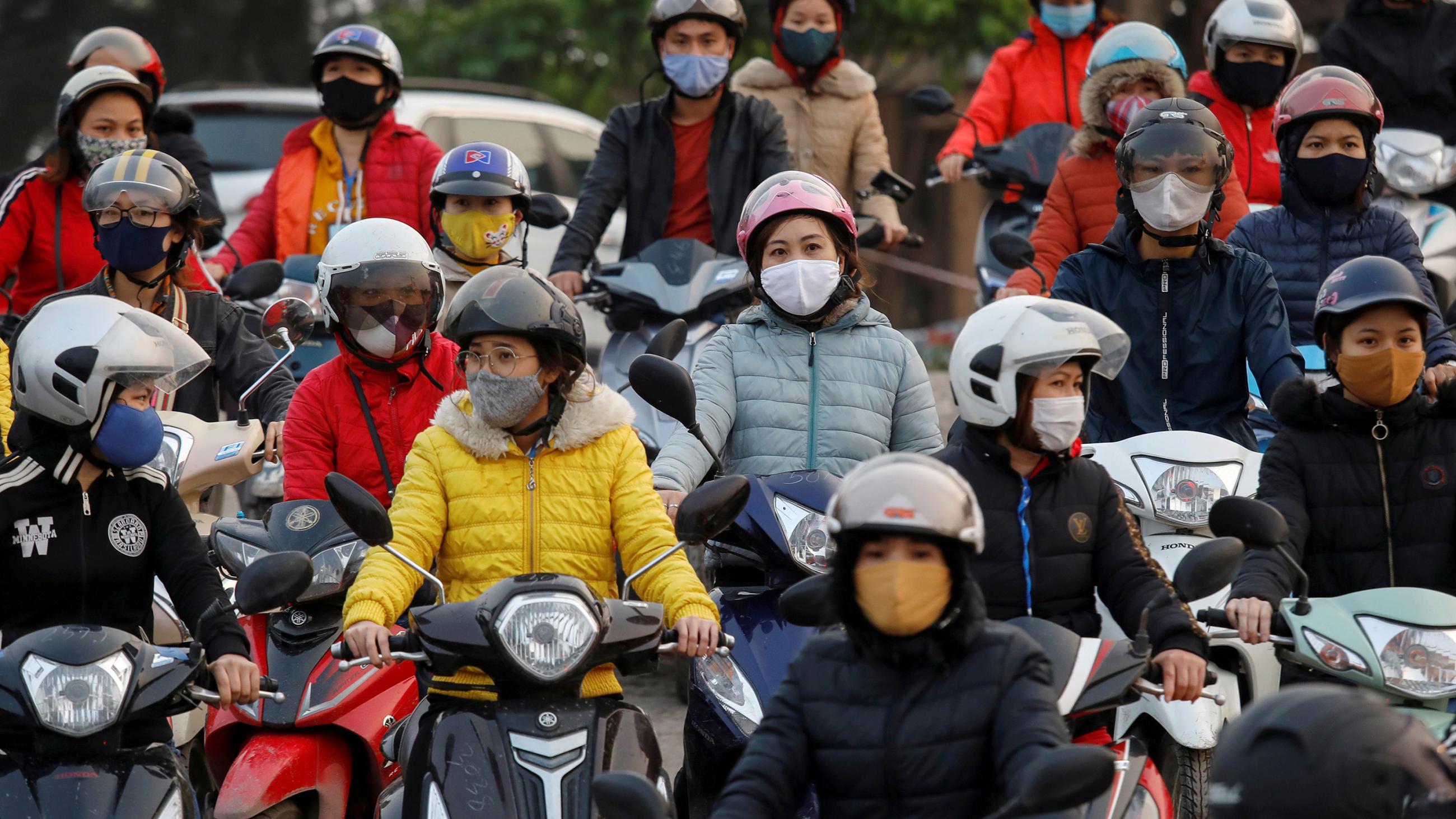 Laborers wearing protective masks gather while they wait for a ferry on the way home after work during the coronavirus outbreak in Hai Duong province, Vietnam, on April 7, 2020. The image shows a number of people on motorcycles wearing masks. 