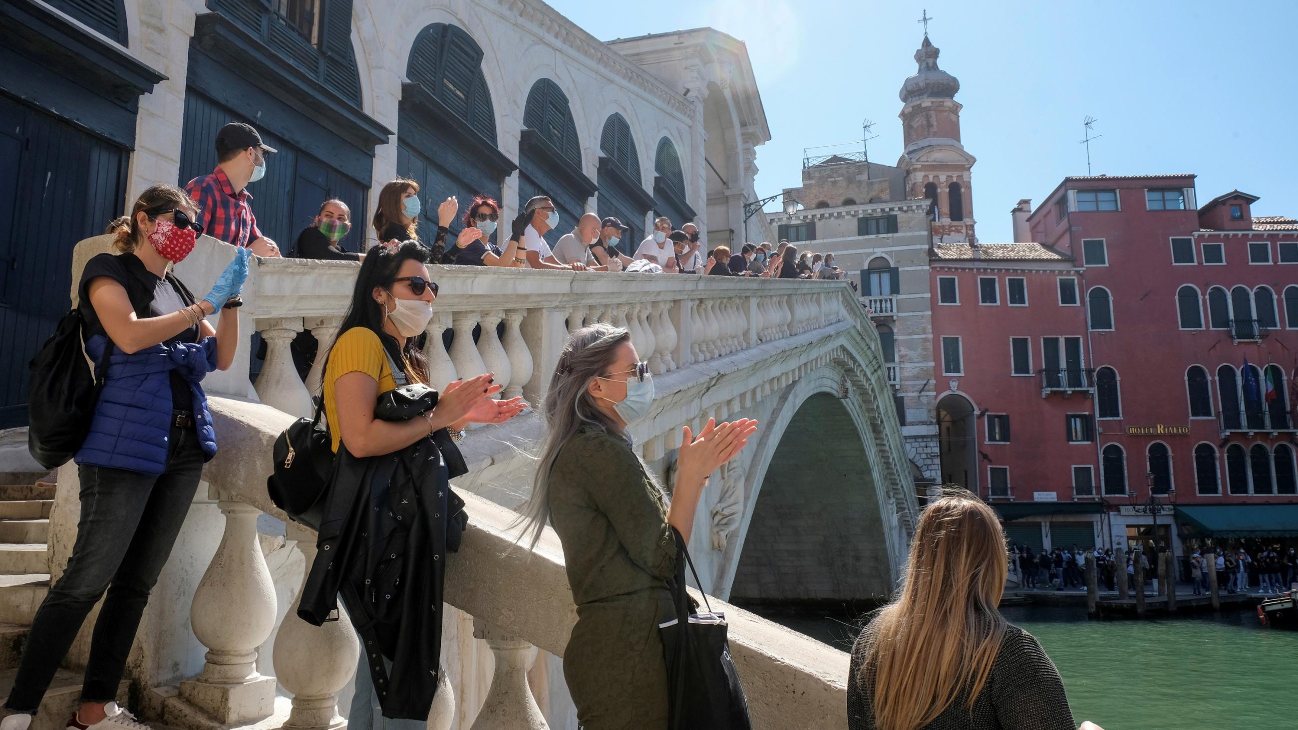 The photo shows a line of people social distancing standing on a picturesque bridge on a beautiful sunny day. 