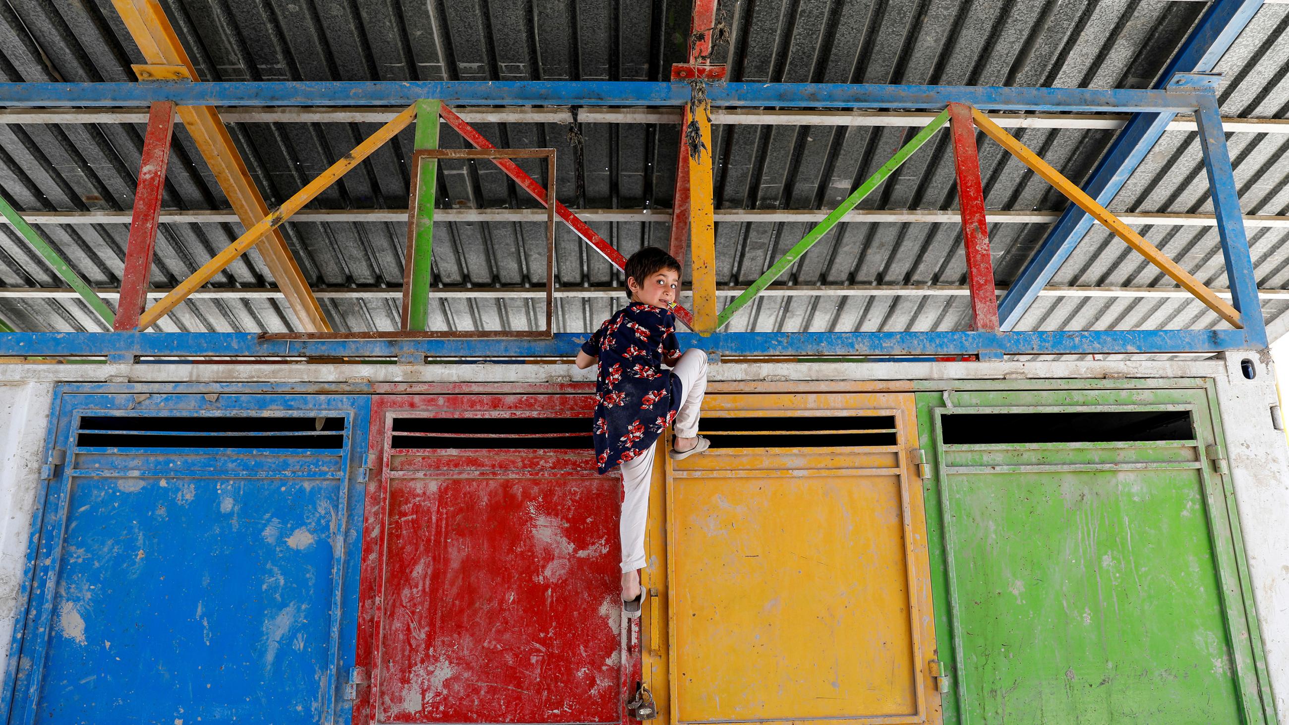 The picture shows a small girl climbing up a brightly colored metal container.