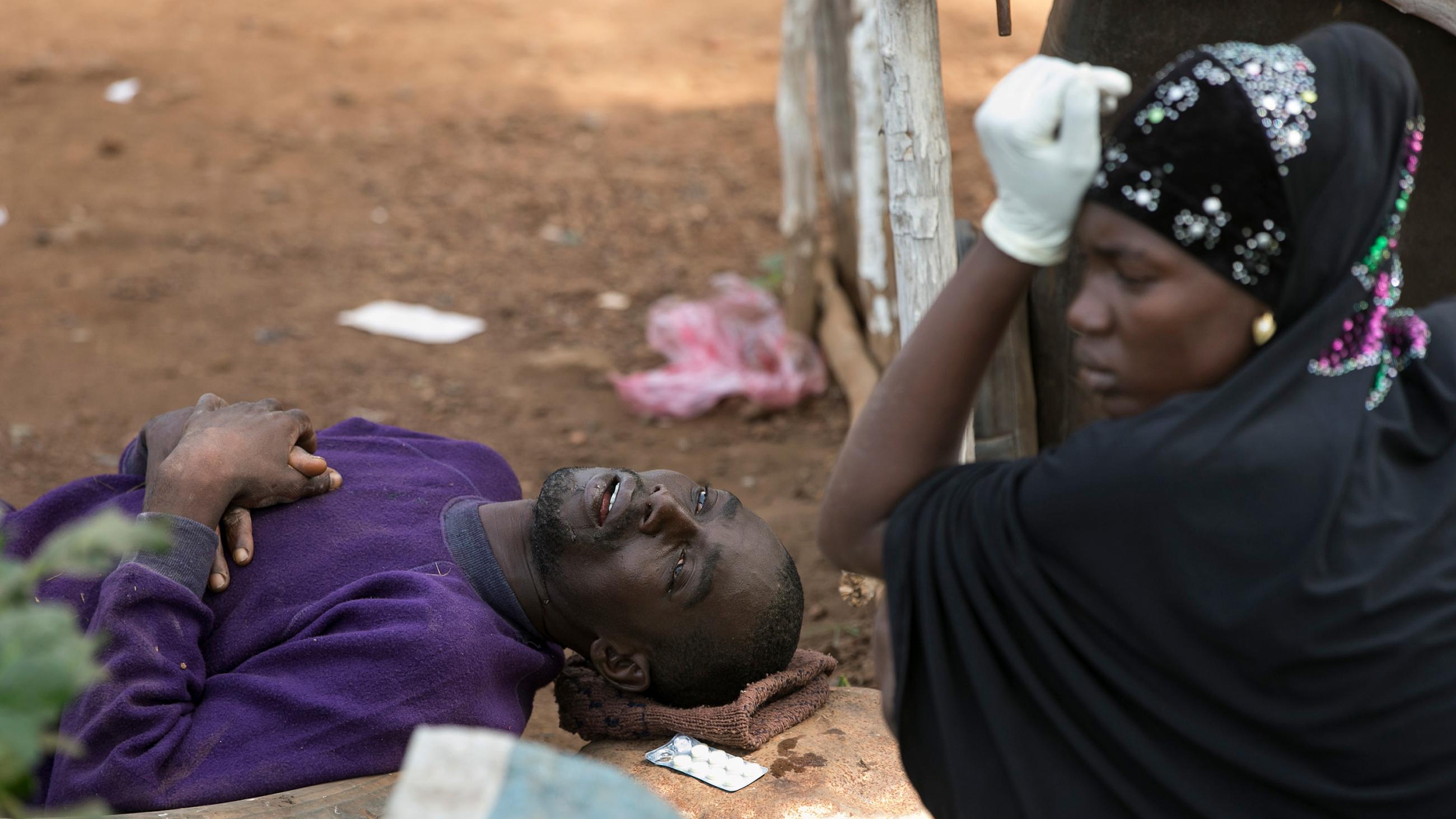The photo shows the man lying on his back, completely out of it, while his wife sits next to him looking tired and worried with her head rested on her hand.