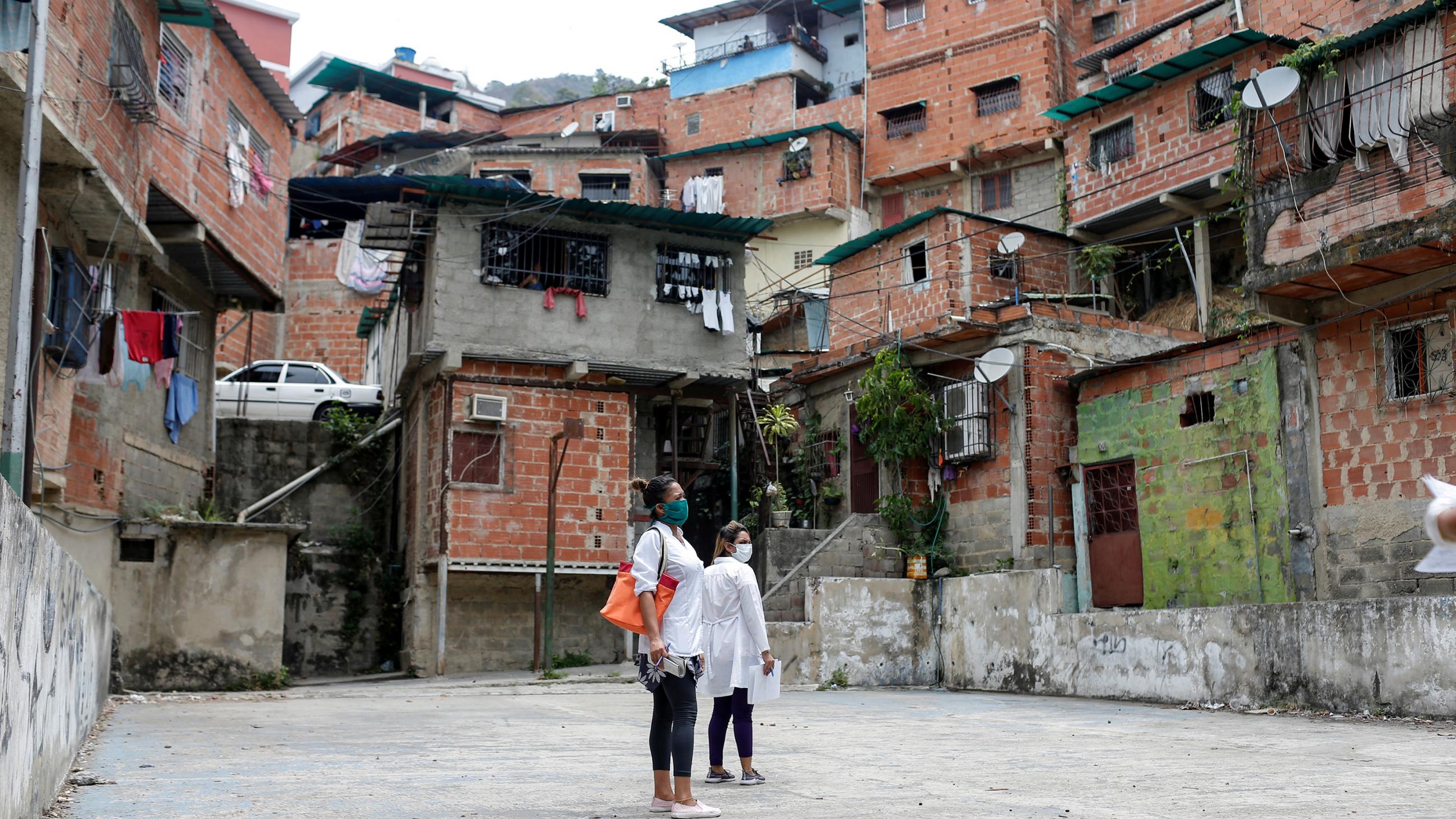 Picture shows two people standing before a huge neighborhood of towering ramshackle structures. 