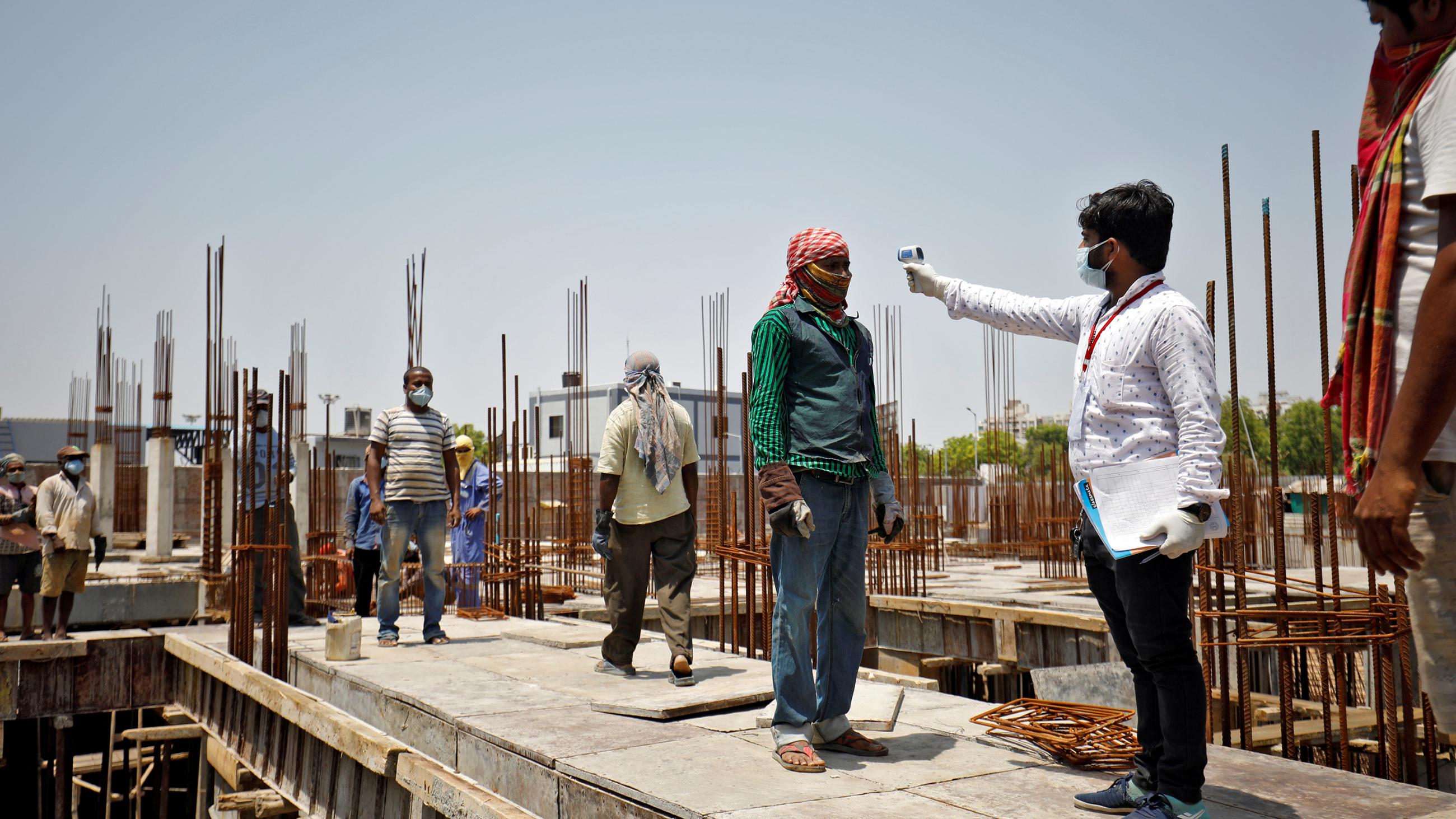 The photo shows the health worker aiming a temperature sensor at the forehead of a construction worker on site at a dig.