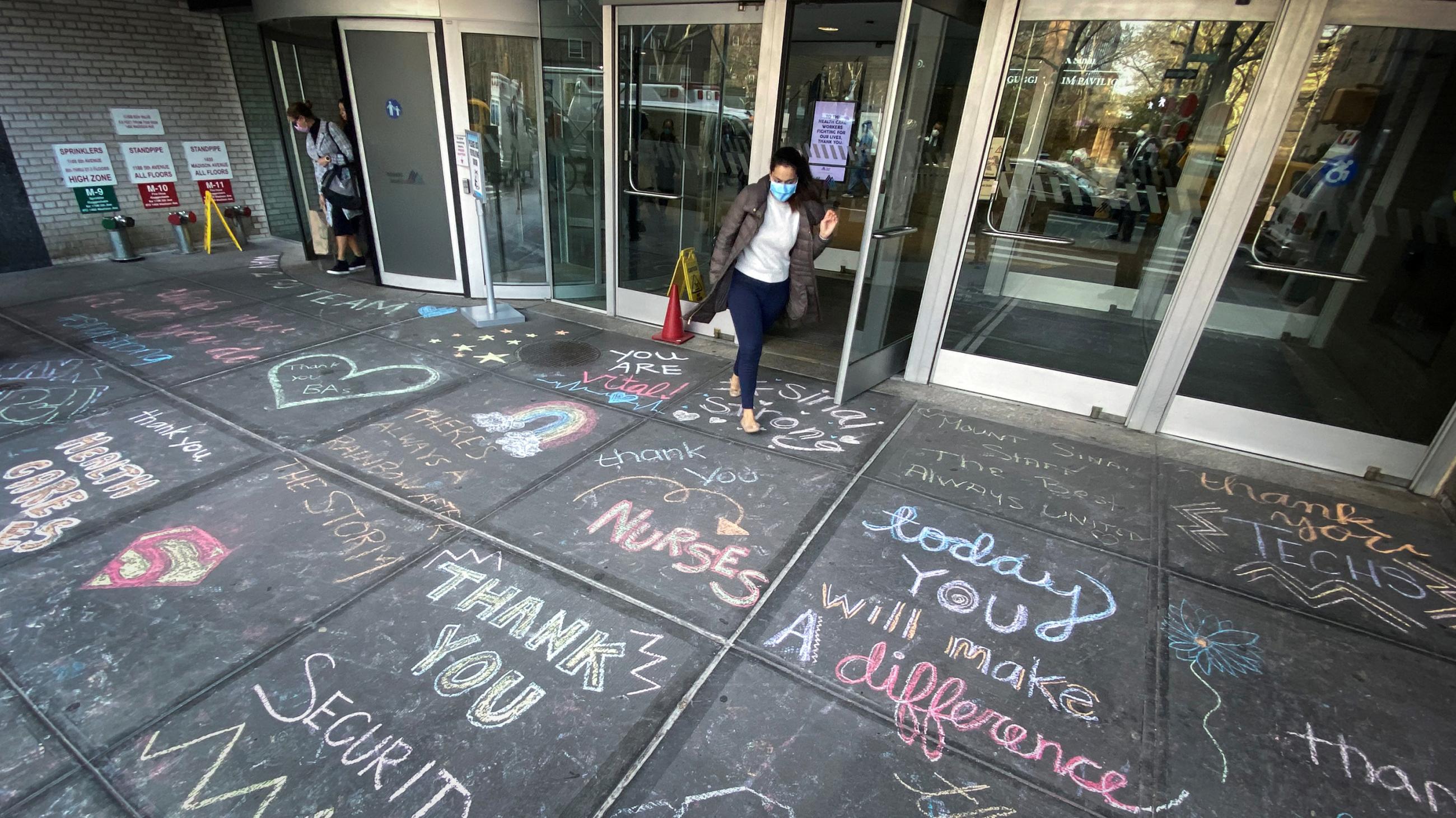 The photo shows an entrance to the hospital with a large number of colorful messages of thanks written in chalk on the sidewalk outside. 