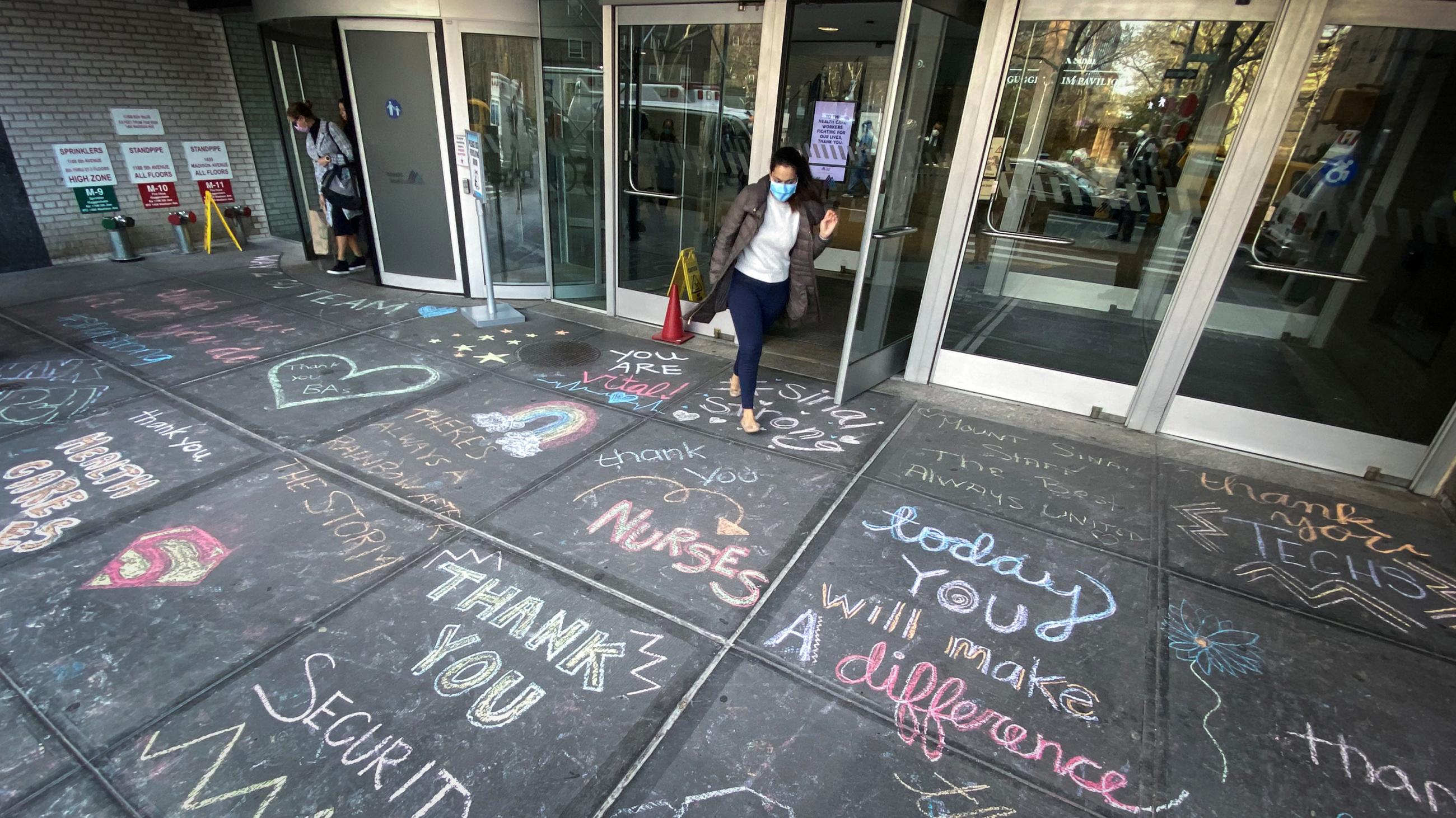 The photo shows an entrance to the hospital with a large number of colorful messages of thanks written in chalk on the sidewalk outside.