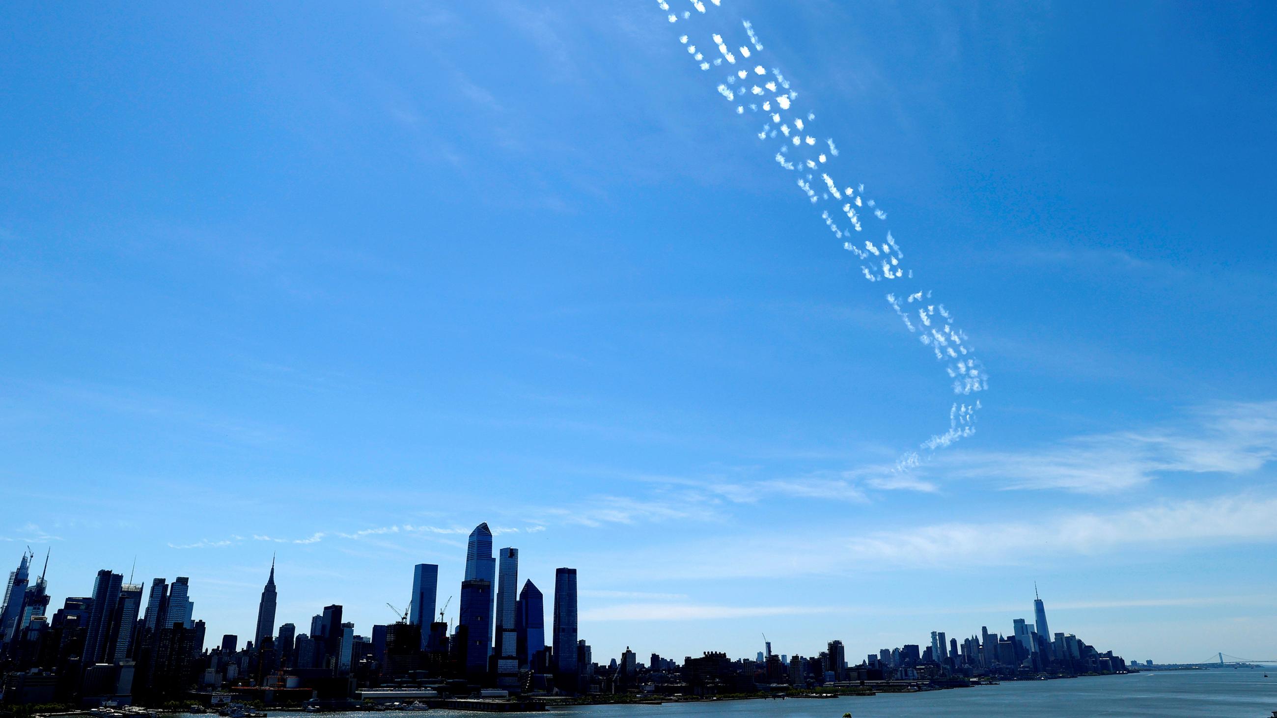 The photo shows the skyline of New York from a distance with a skywriting message visible above the city on a crystal-clear, blue-sky day. 