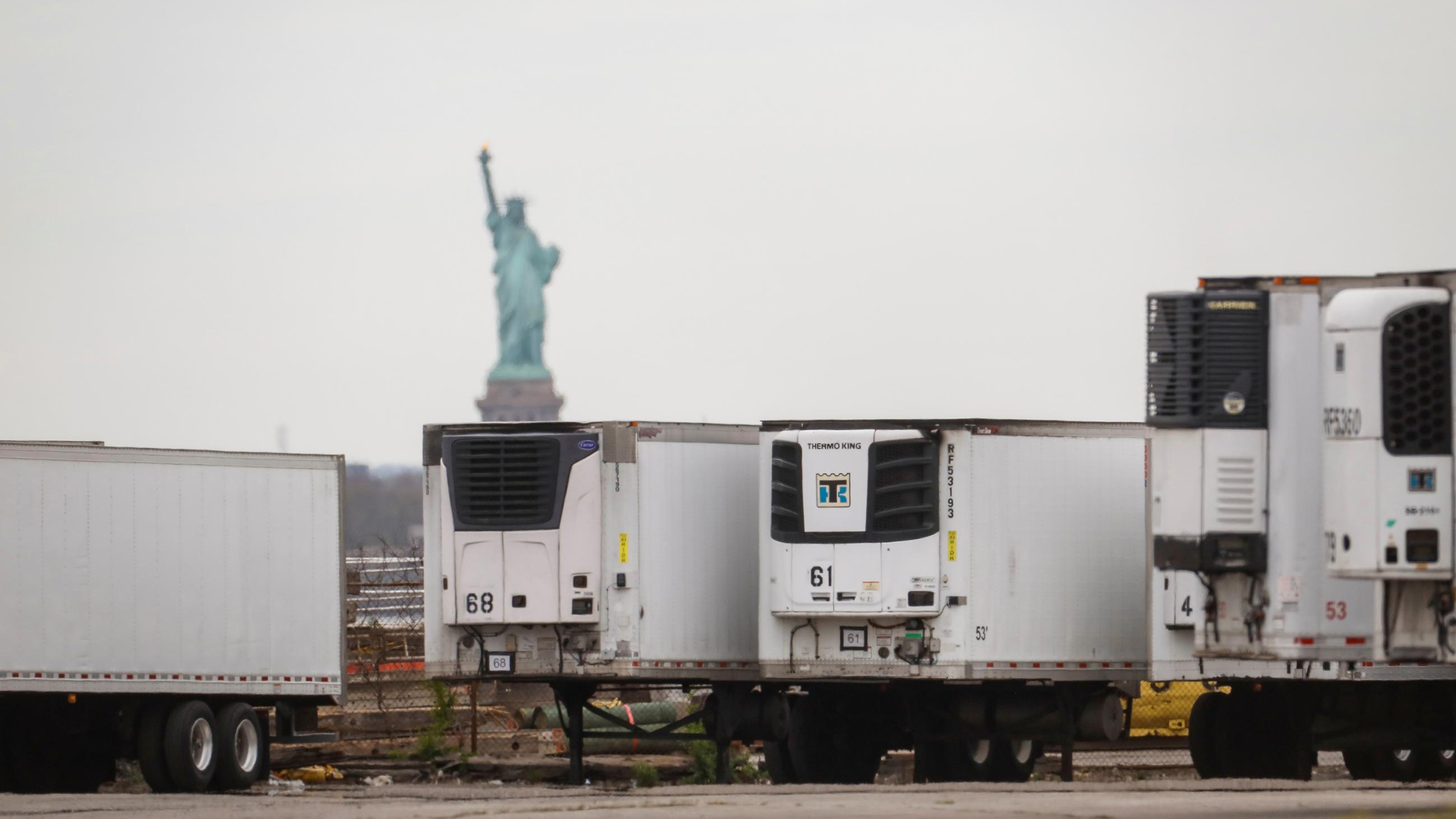 The photo shows several large 18-wheeler trucks parked with the Statue of Liberty in the background. 