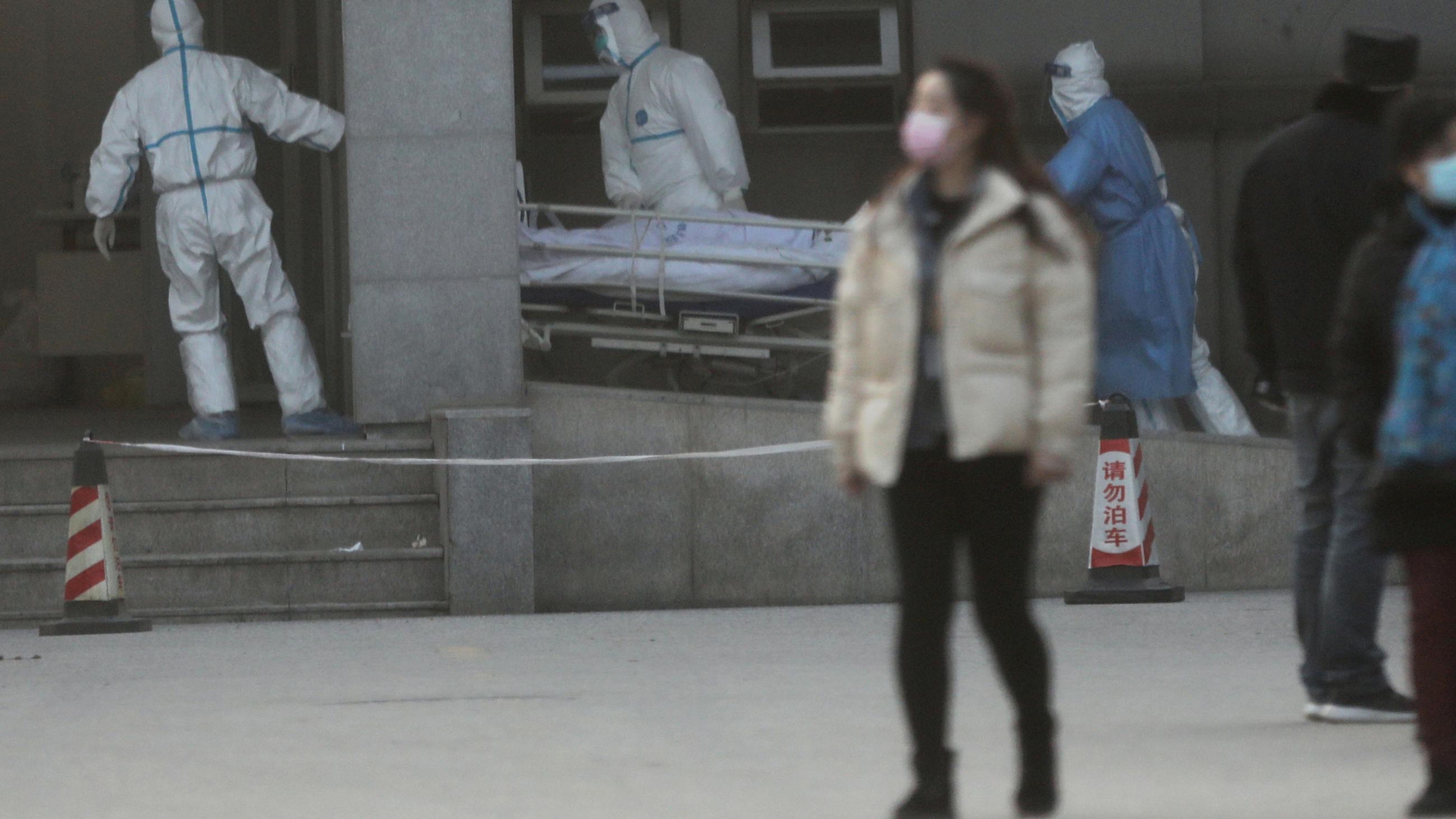 The photo shows an entrance to a hospital with a few workers wheeling a patient across the drive. 