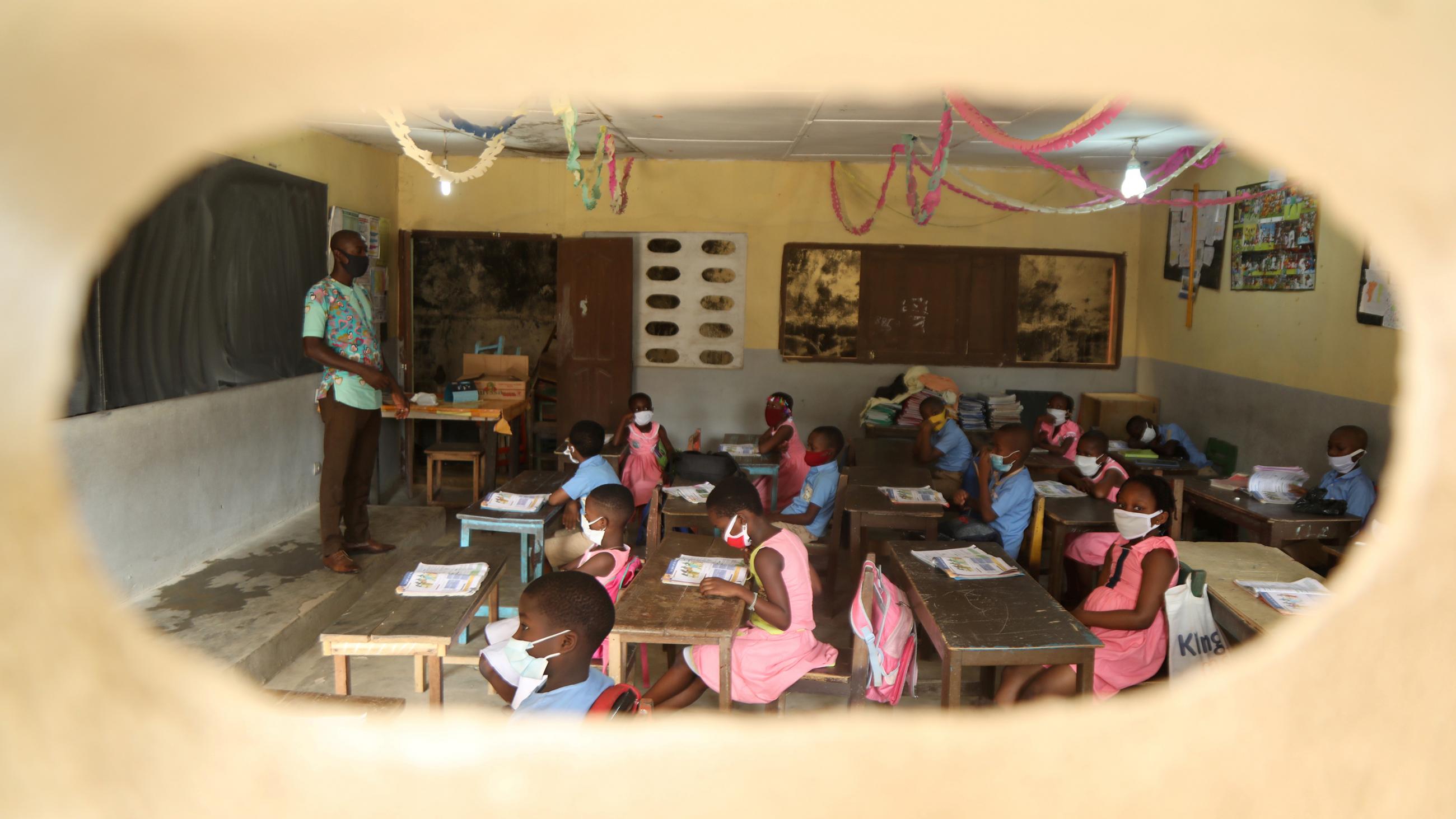 The image shows a classroom shown through a window. 