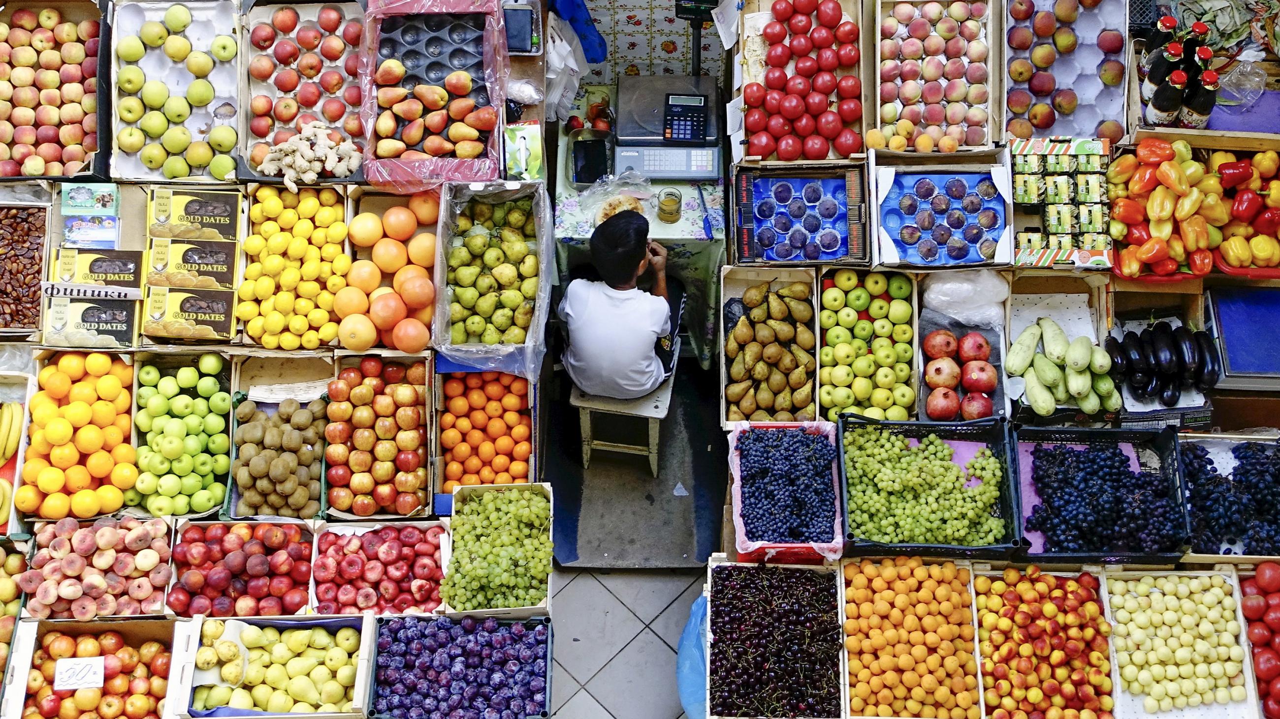 The photo shows a boy taking a break eating his lunch amid a fruit stand. 