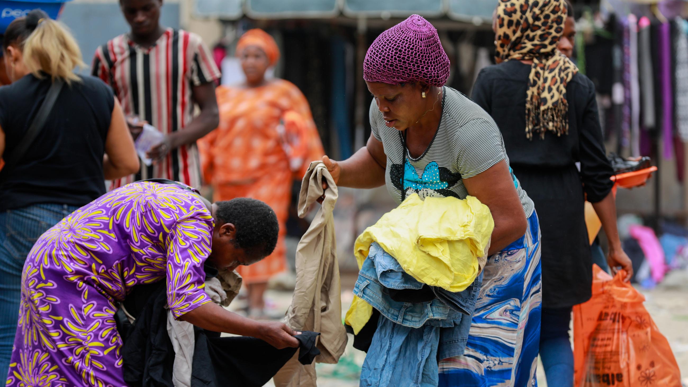 Picture shows a number of women with shopping bags and armfuls of clothes in an open market. 