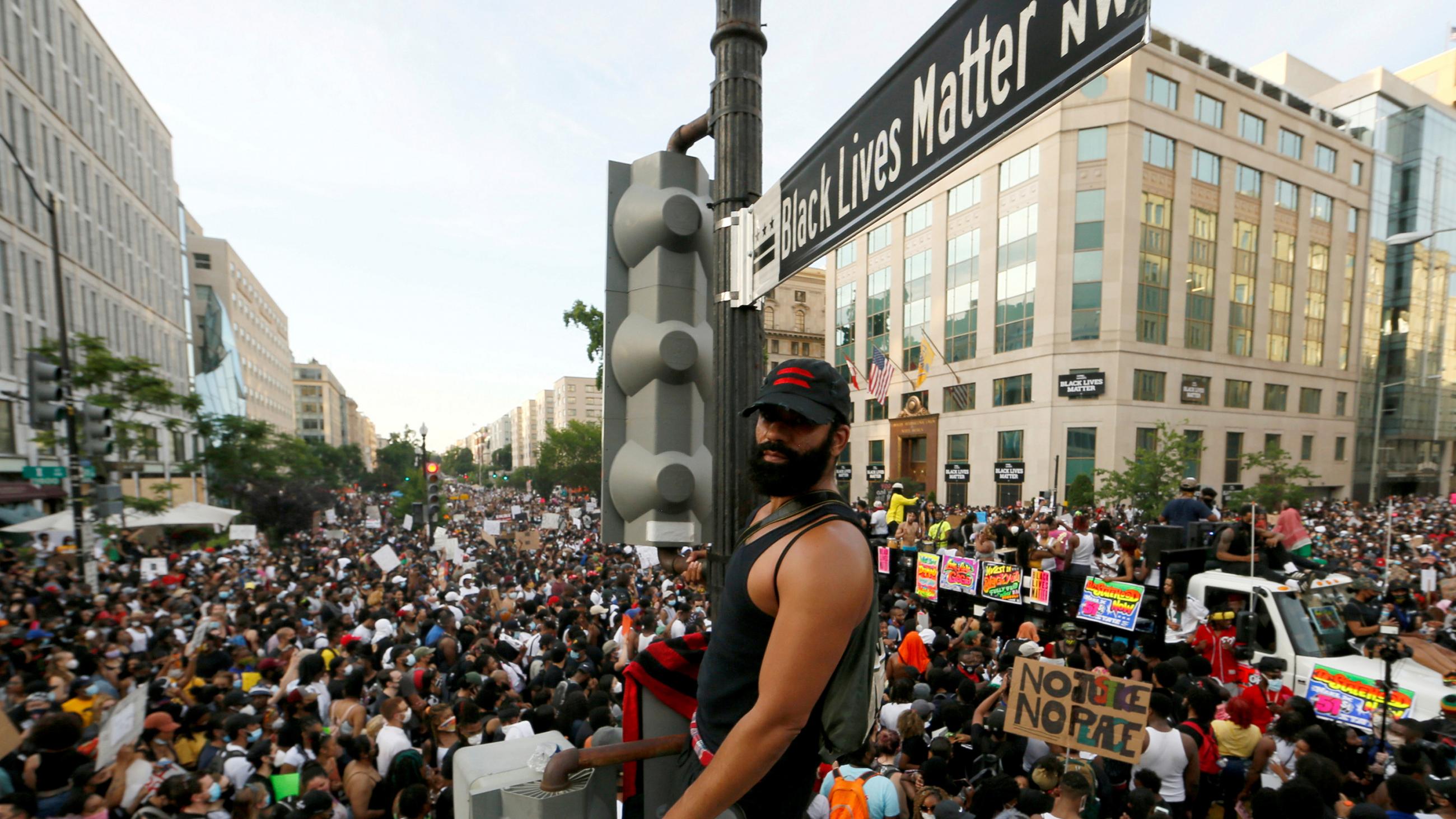 The photo shows the protestor standing on the light post above a massive crowd.