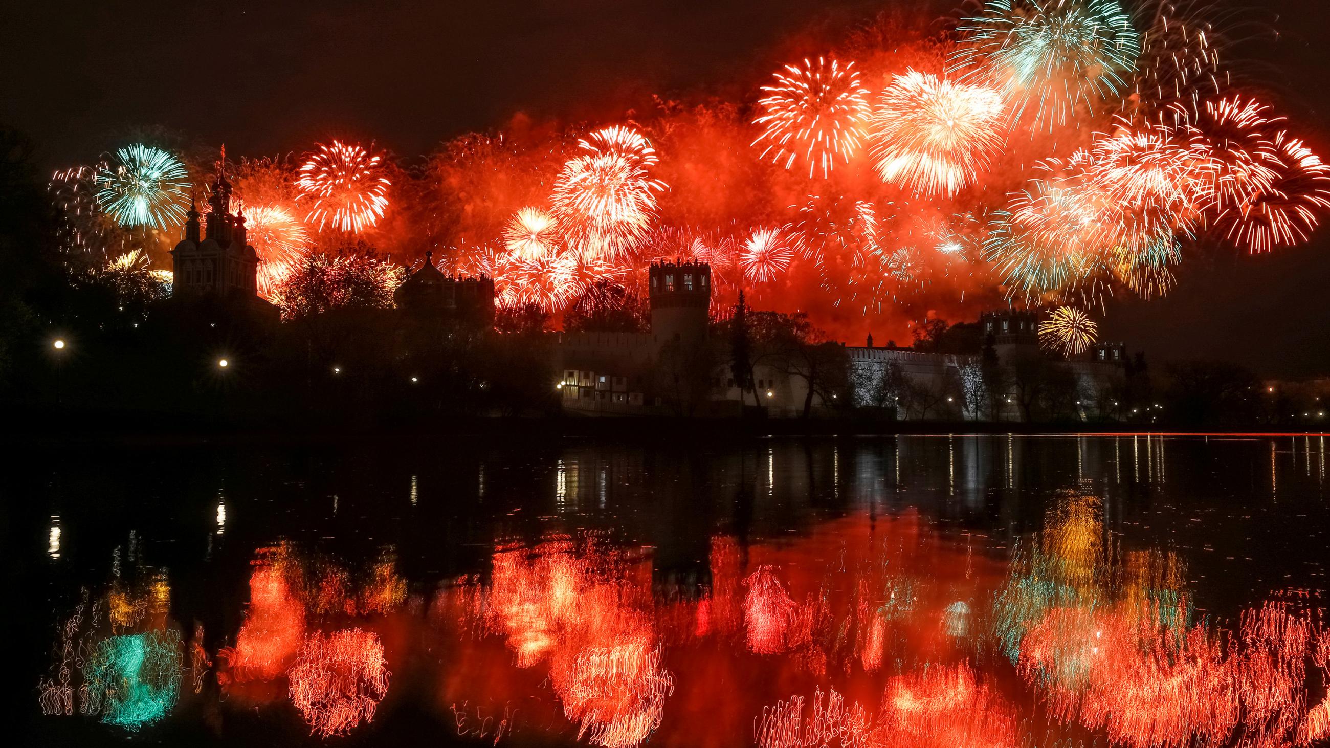 This is a striking photo showing a huge number of fireworks exploding behind a magnificent monastery and reflected on the river facing the camera. 