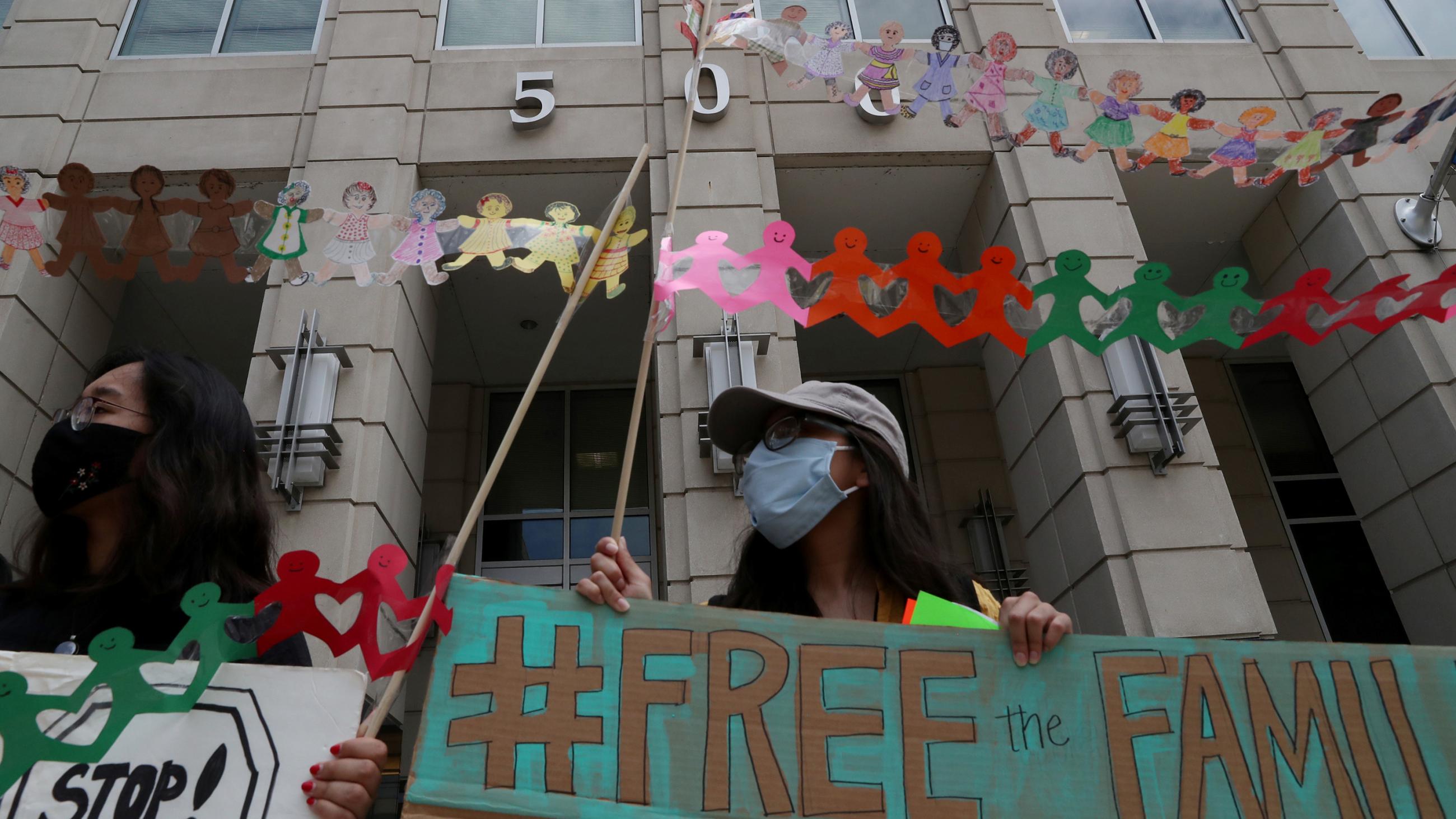 The photo shows a protester wearing a mask and holding a sign that "#FREE THE FAMILY." 