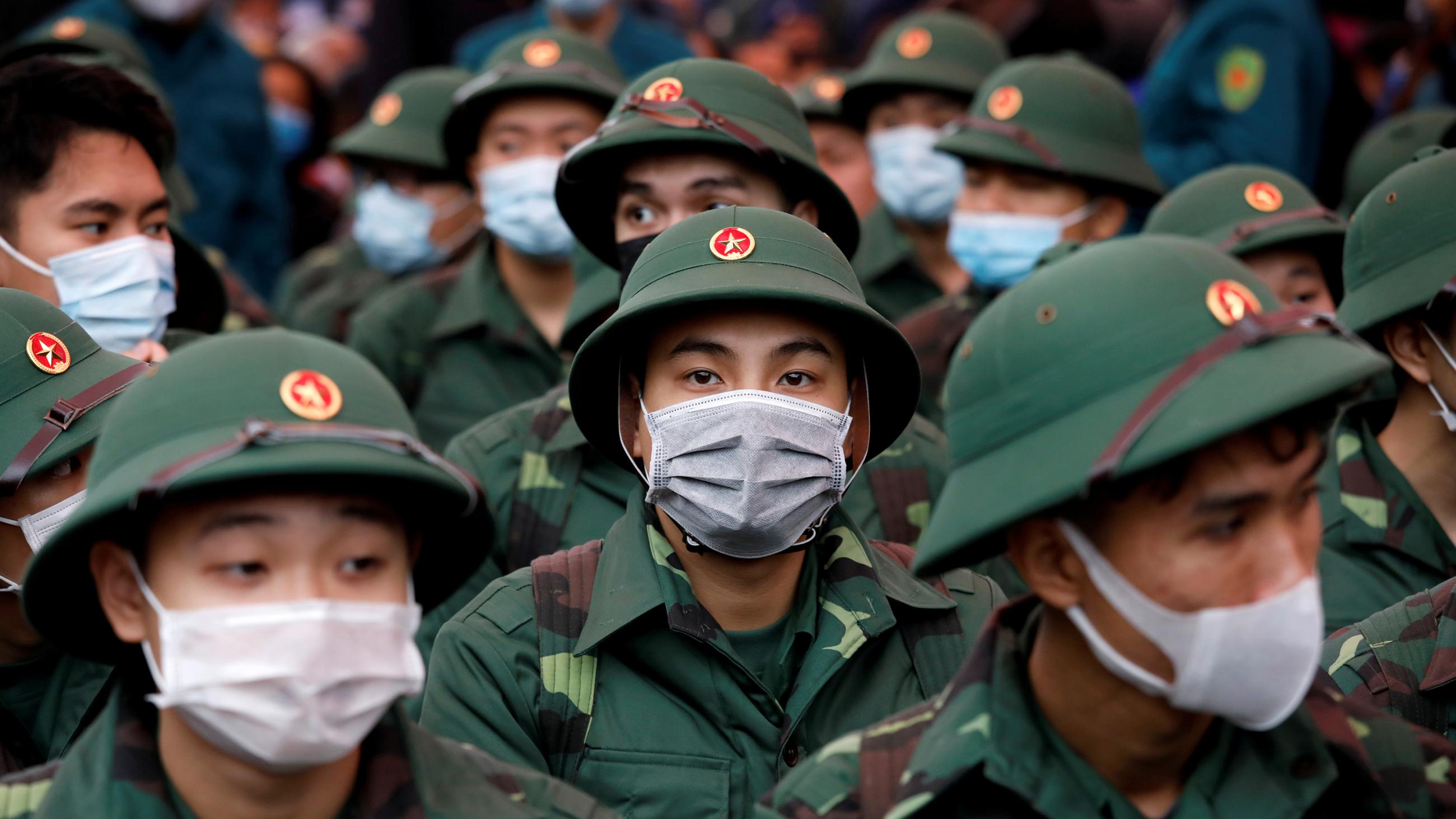 The photo shows a crowd of soldiers in their green dress uniforms all wearing masks. 