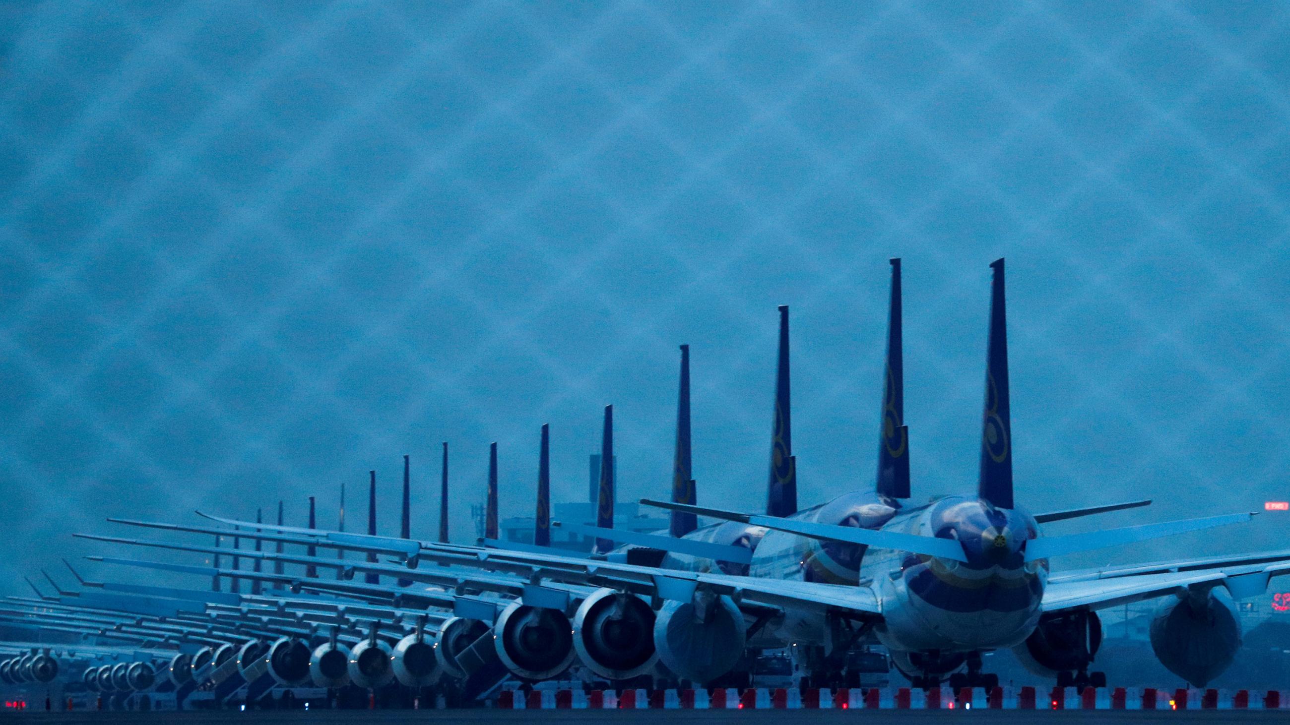 The photo shows a row of airplanes at dusk in a dark blue light. 