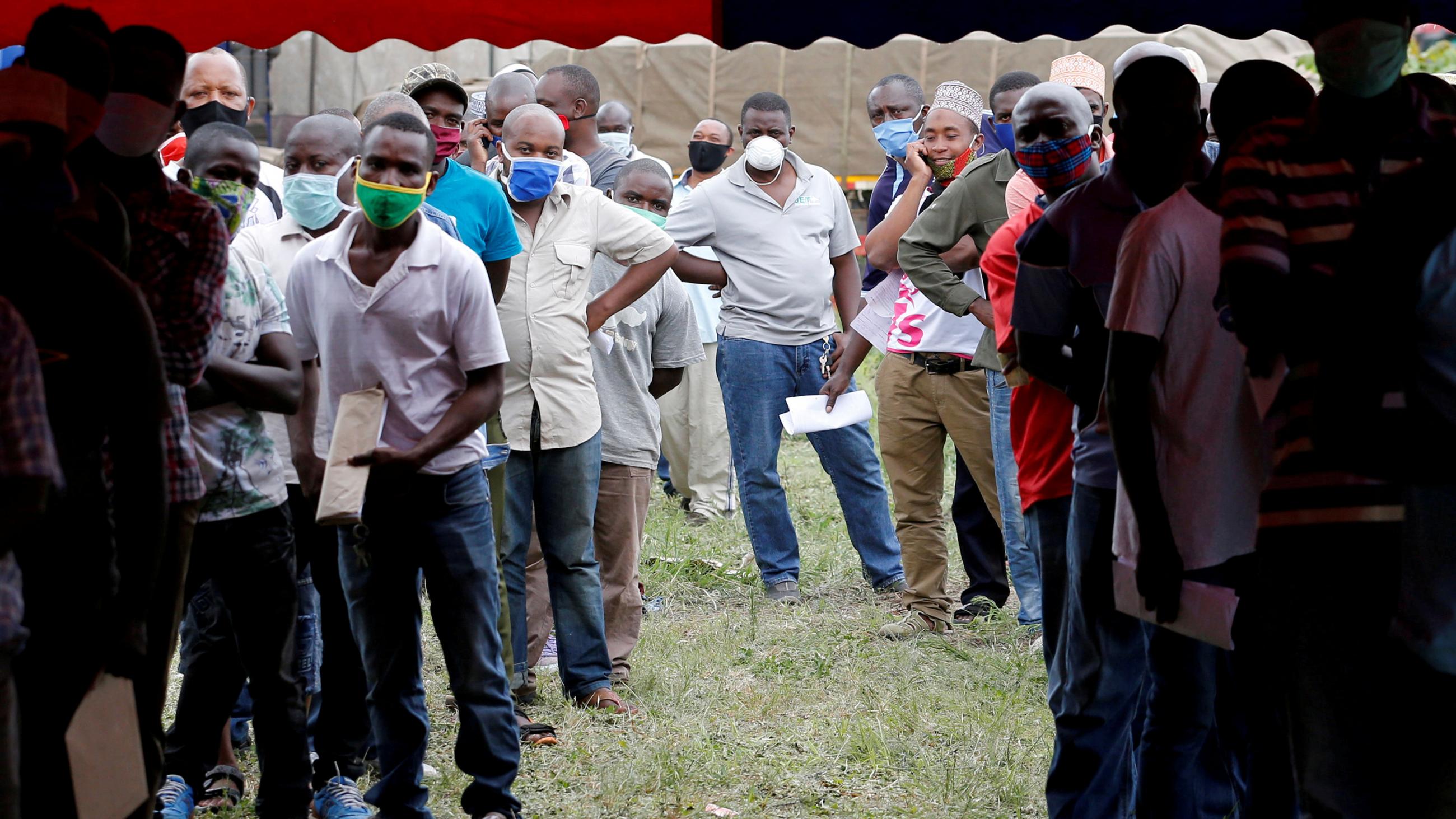 The image shows a long line of truck drivers standing in a line and waiting. 