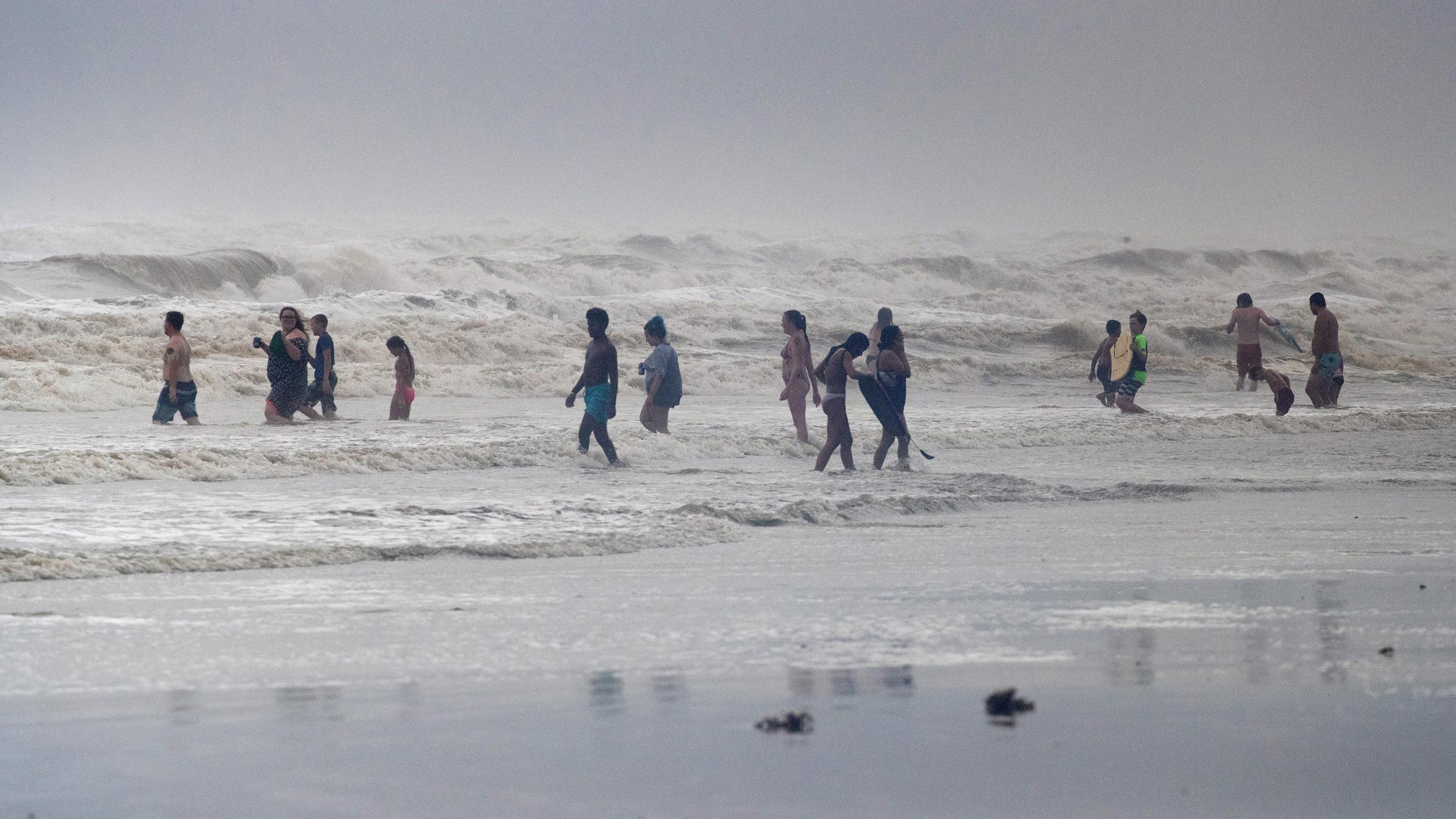 The photo shows a number of people on a beach amid huge waves. 
