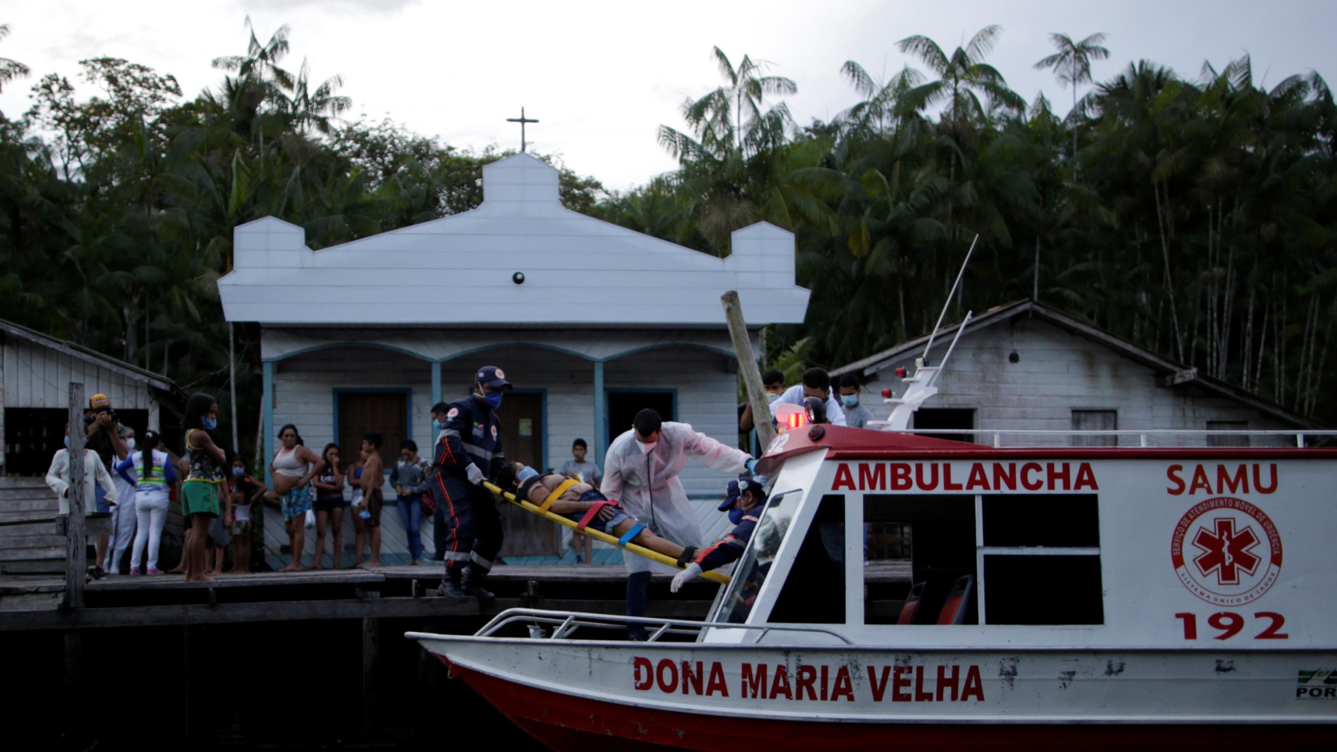 The photo shows a riverboat painted in ambulance colors docked at a river stop at dusk to complete the transfer with numerous onlookers.