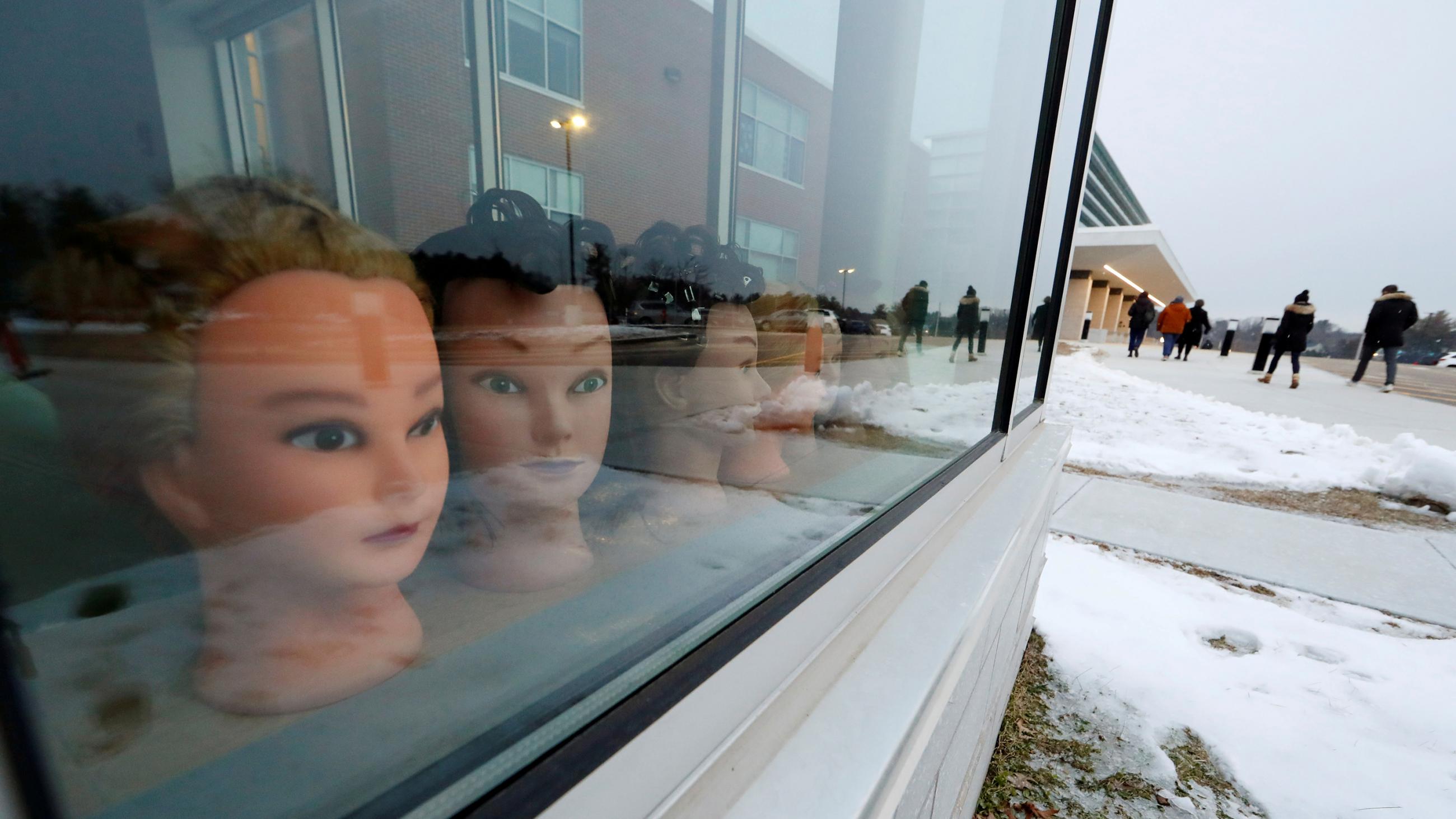 The photo shows a bunch of mannequin heads lined up as if they are looking out a window onto a winter scene with kids playing in a snow-covered field. 