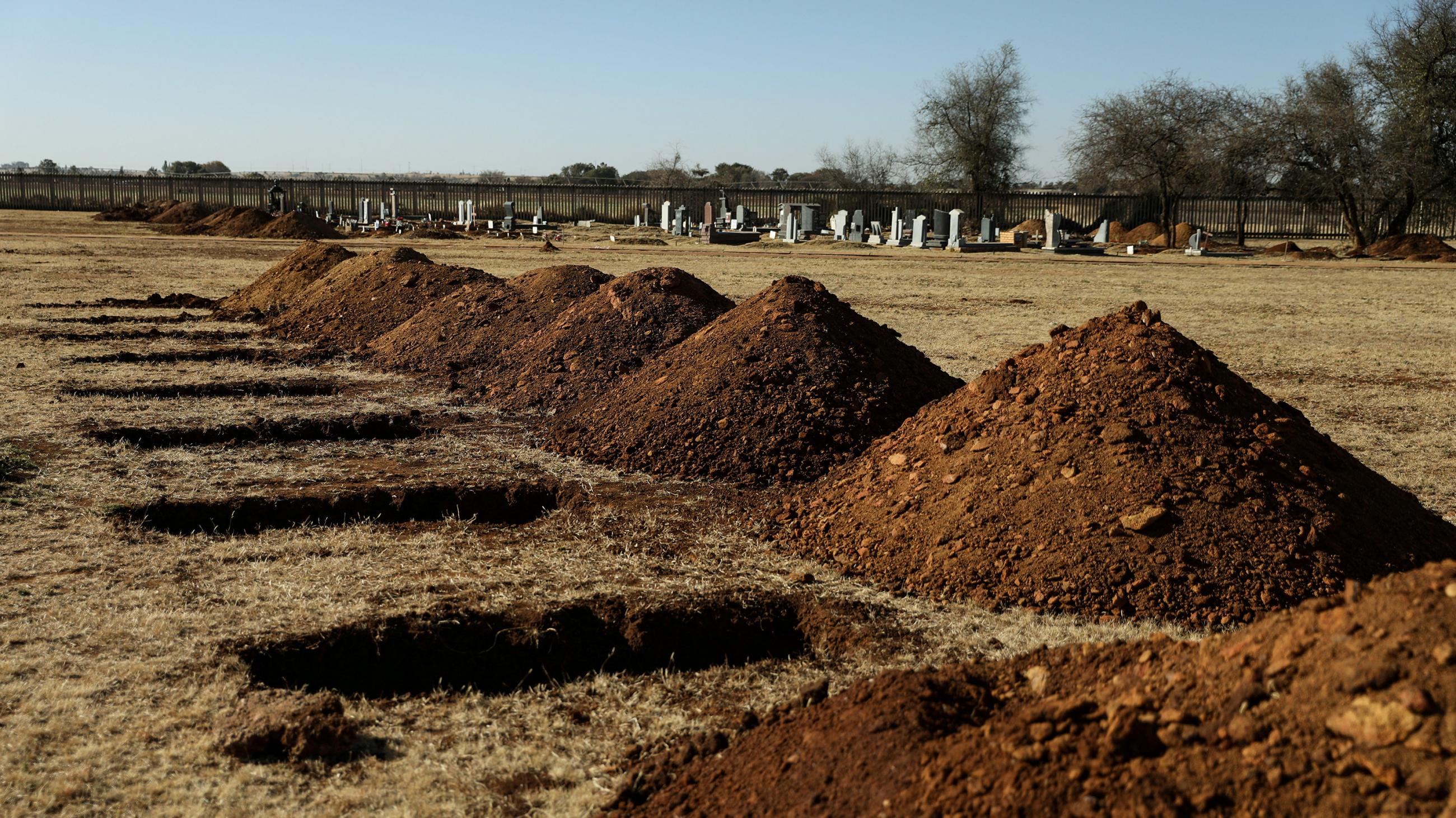 The photo shows a row of graves with mounds of dirt piled beside them. 