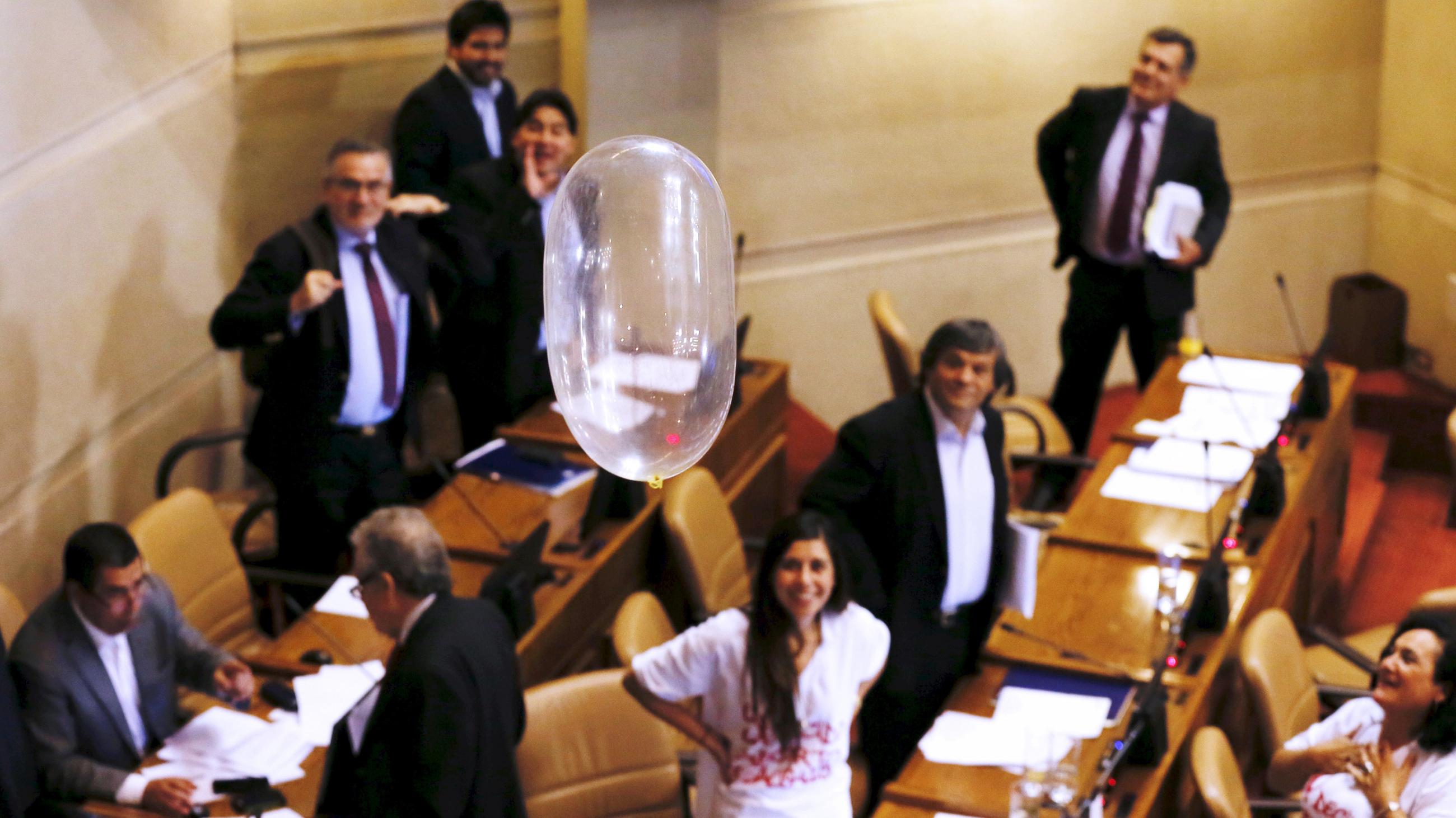 The photo shows several members of congress in their seating standing and looking amused as a blown-up condom can be seen in the foreground. 
