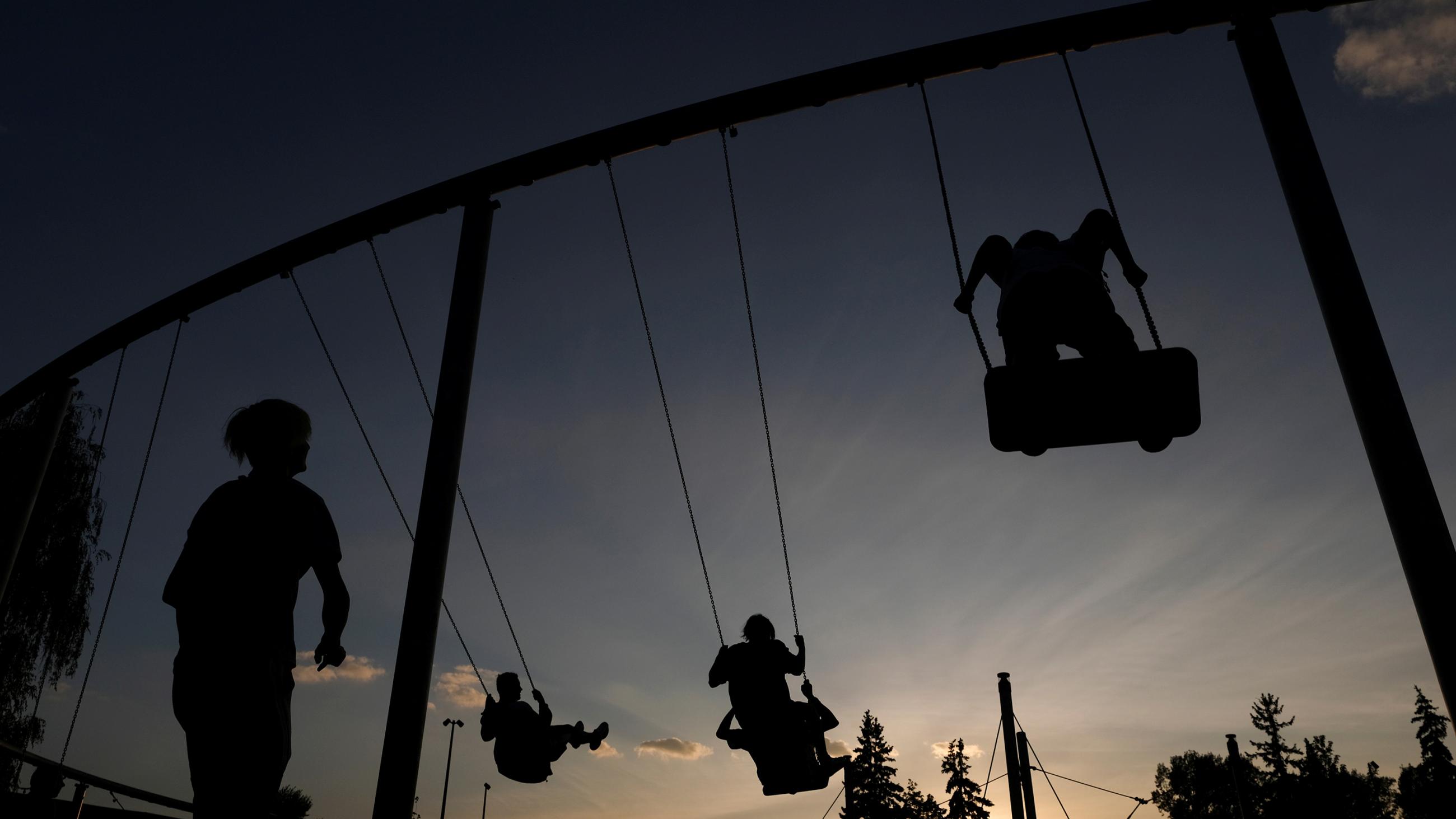 The photo shows a wide-angle shot taken behind a swing set at dusk.