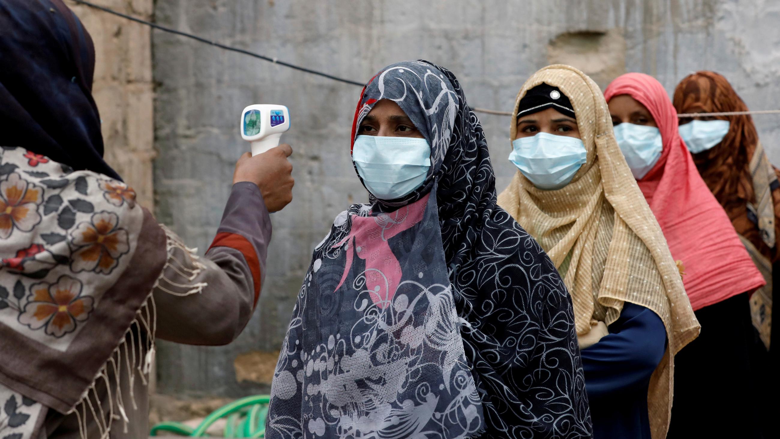 The photo shows several people lined up while their temperature is being checked.