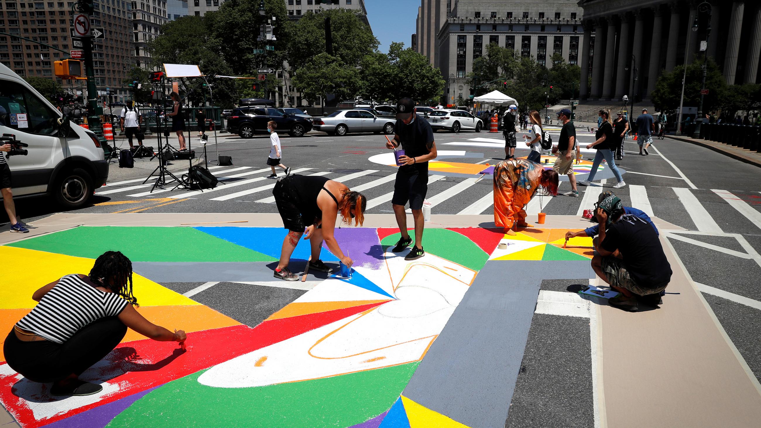 The photo shows people in the streets paining a colorful mural on the ground. 