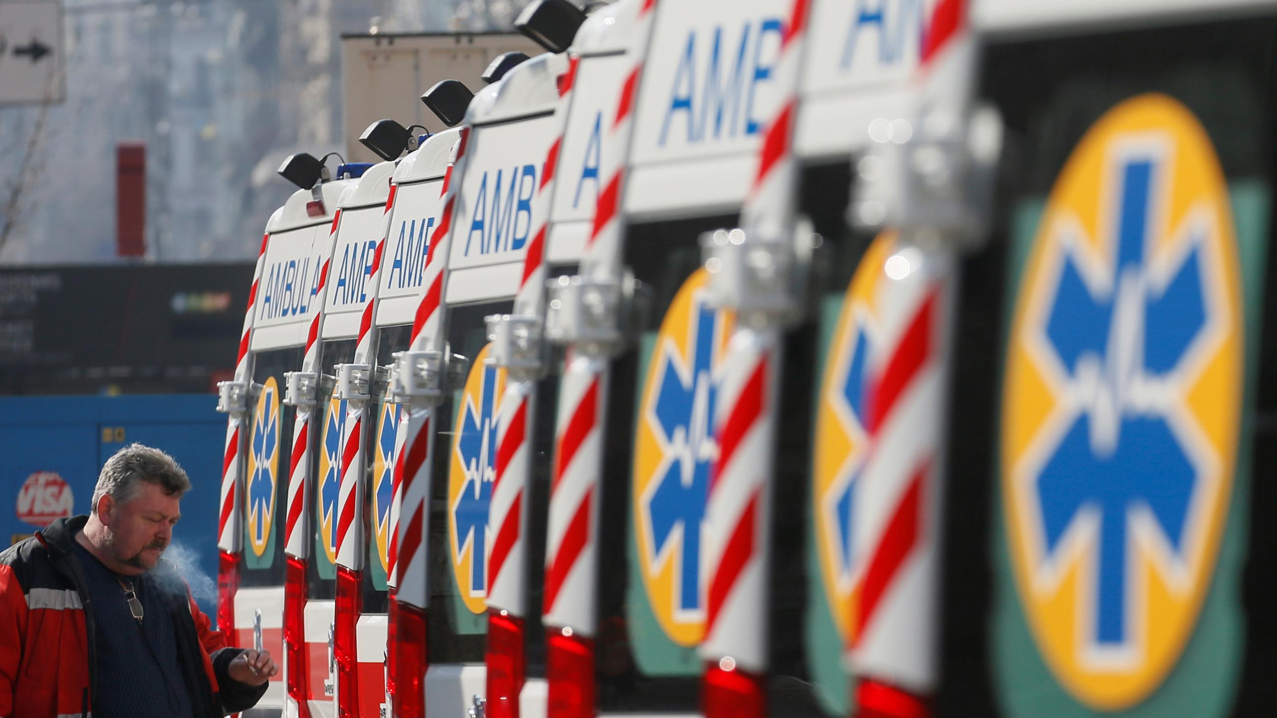 The photo shows a long line of ambulances with a worker at the end puffing on a cigarette. 
