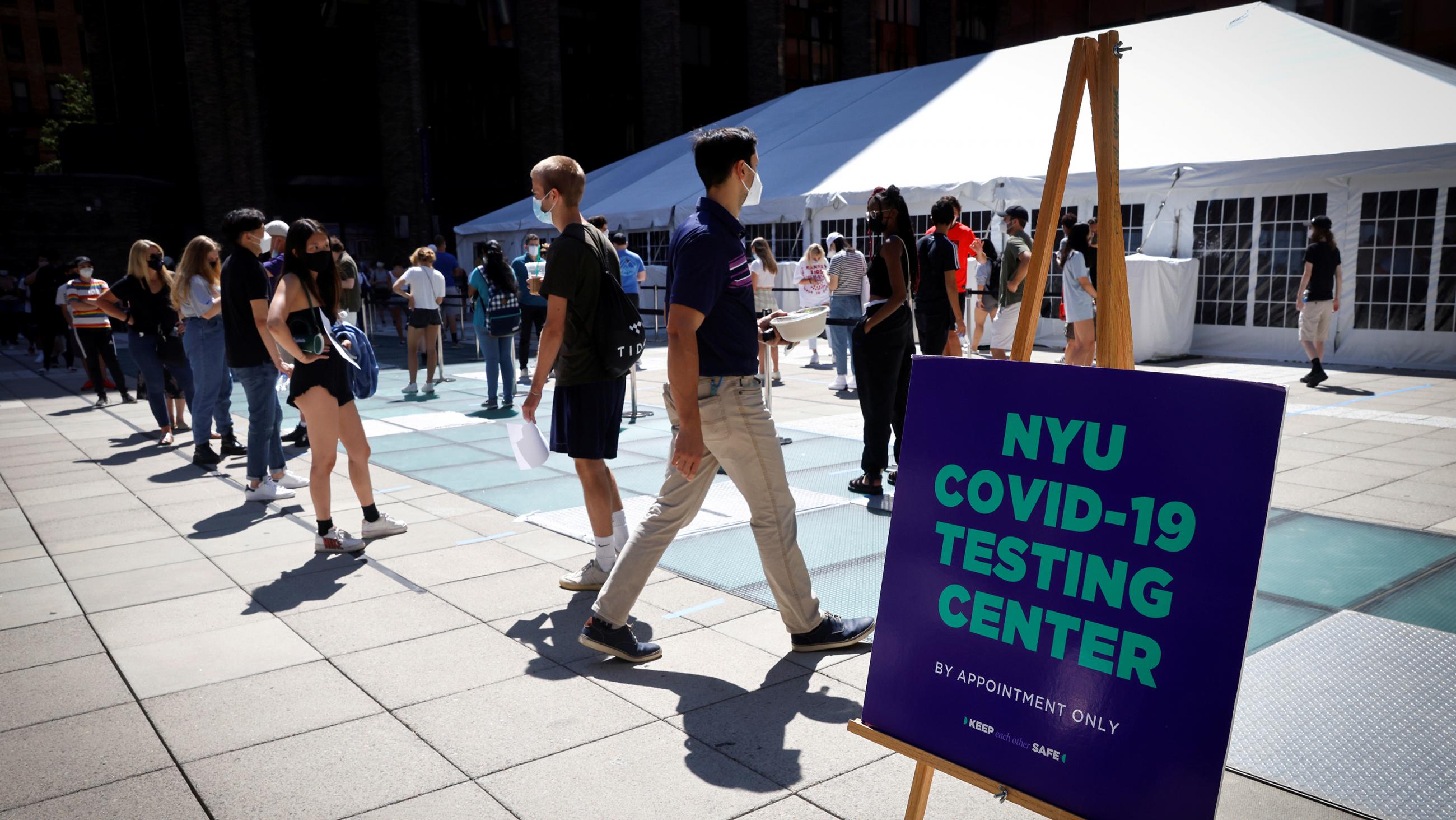 The photo shows several people standing around in line with a sign nearby announcing the testing.