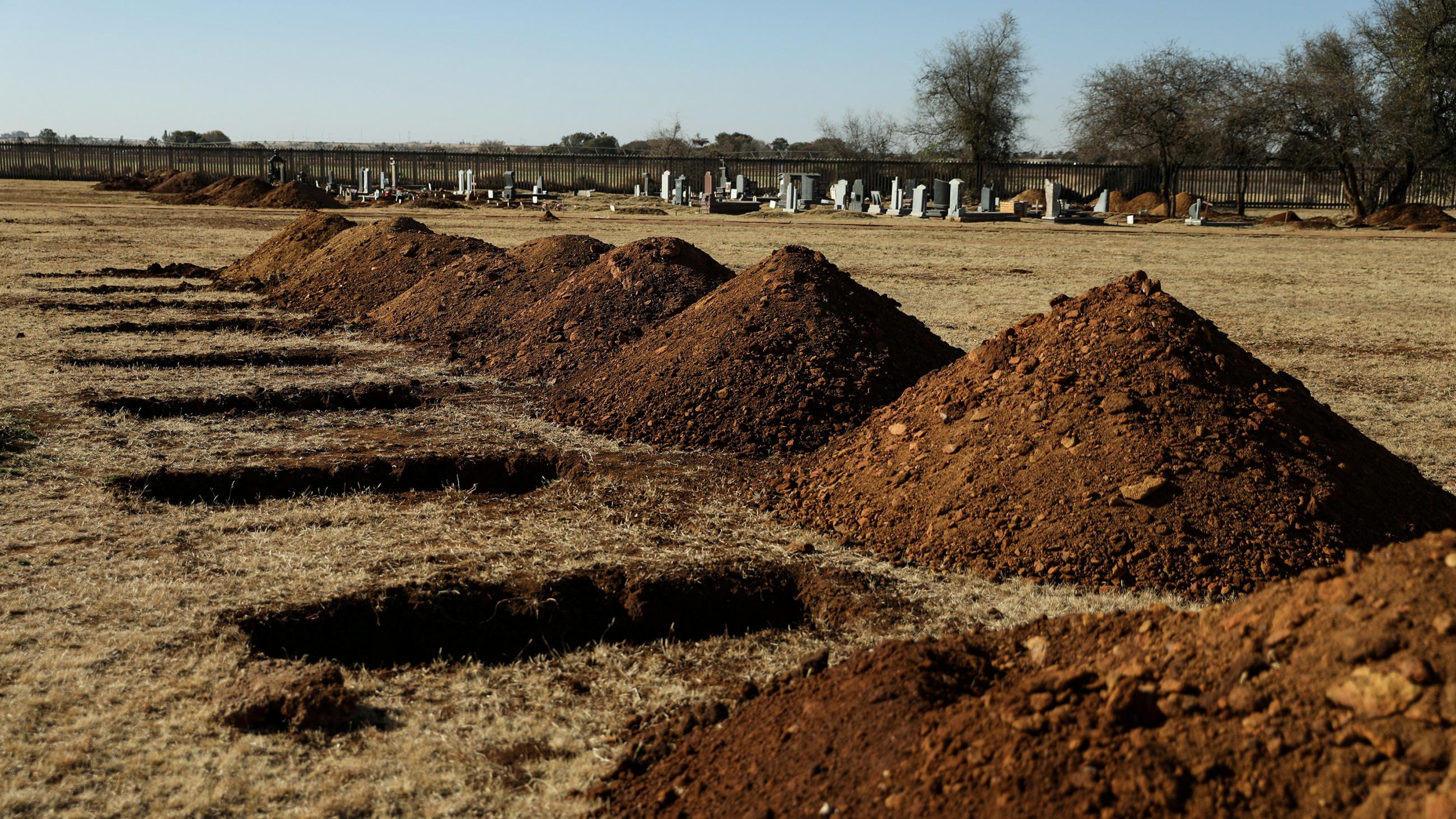 The photo shows mounds of freshly turned dirt next to open graves. 