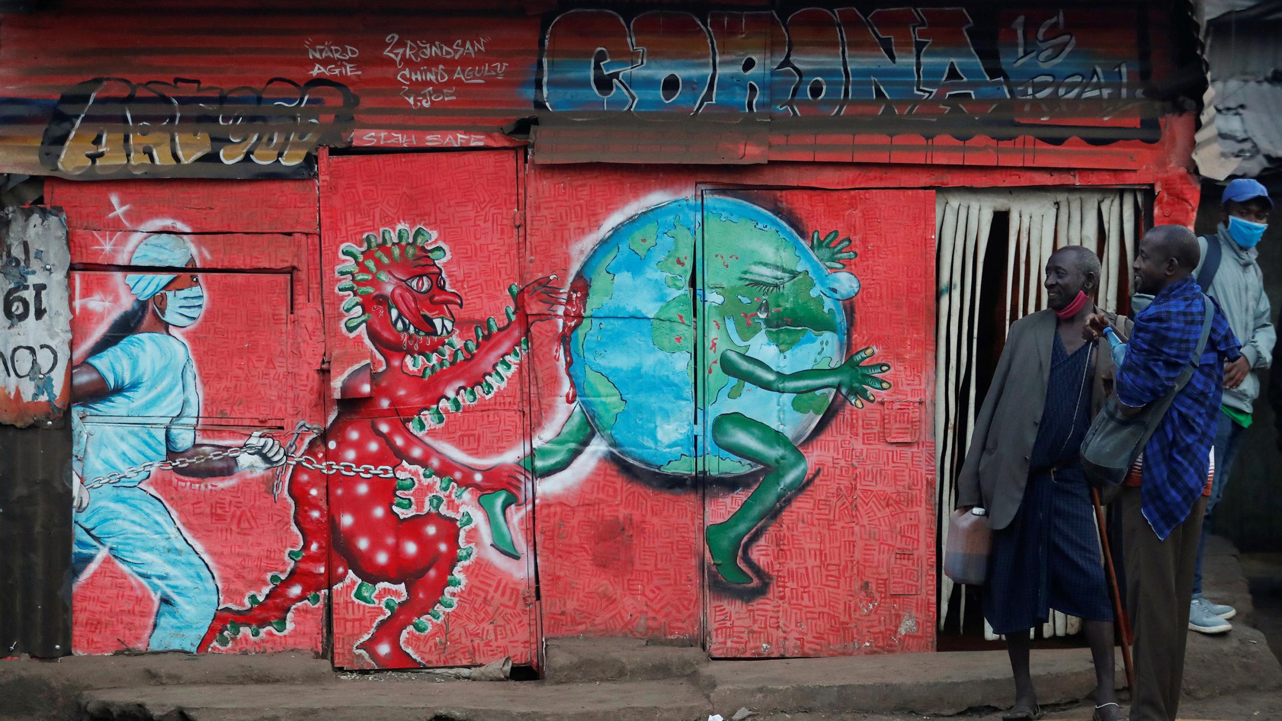 The photo shows a few people milling ablut the entrance of a building on the side of which is painted a mural with a red figure representing the personification of coronavirus chasing a globe while a nurse follows behind in hot pursuit.