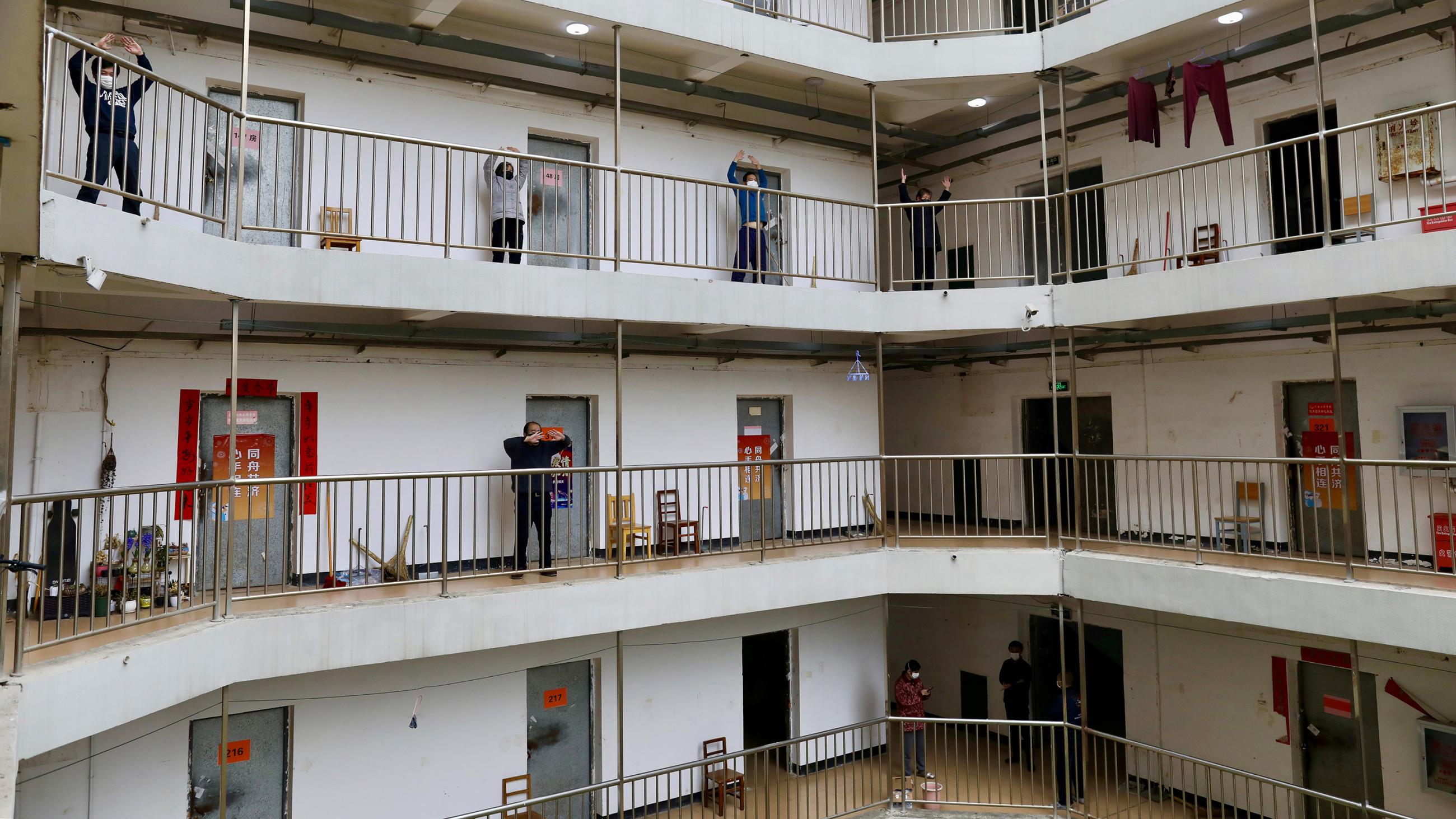 The photo shows multiple levels of an apartment building-type structure with several people on one of the floors exercising in the open-air walkway.
