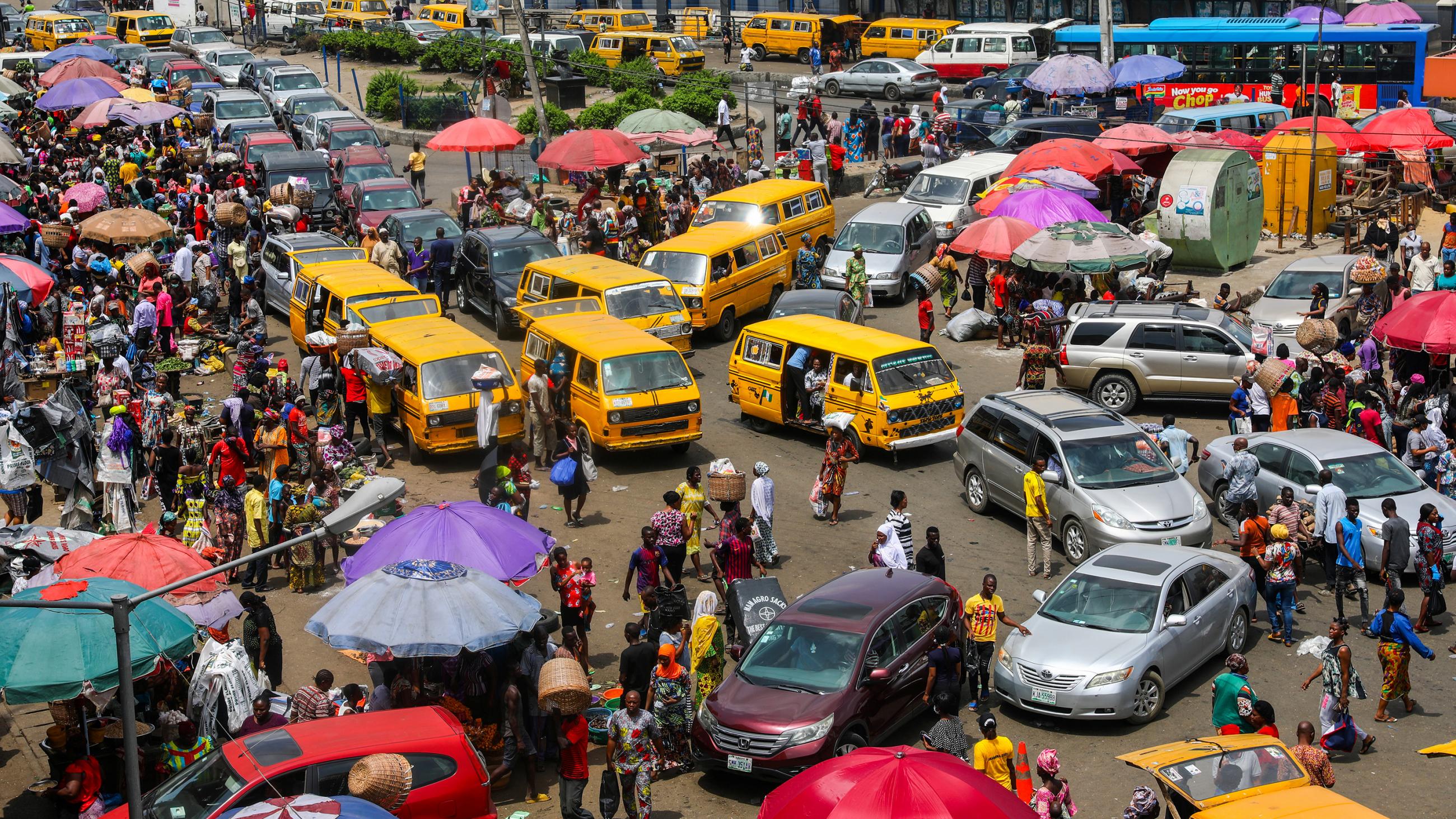 The photo shows a bustling market crowded with people and cars. 