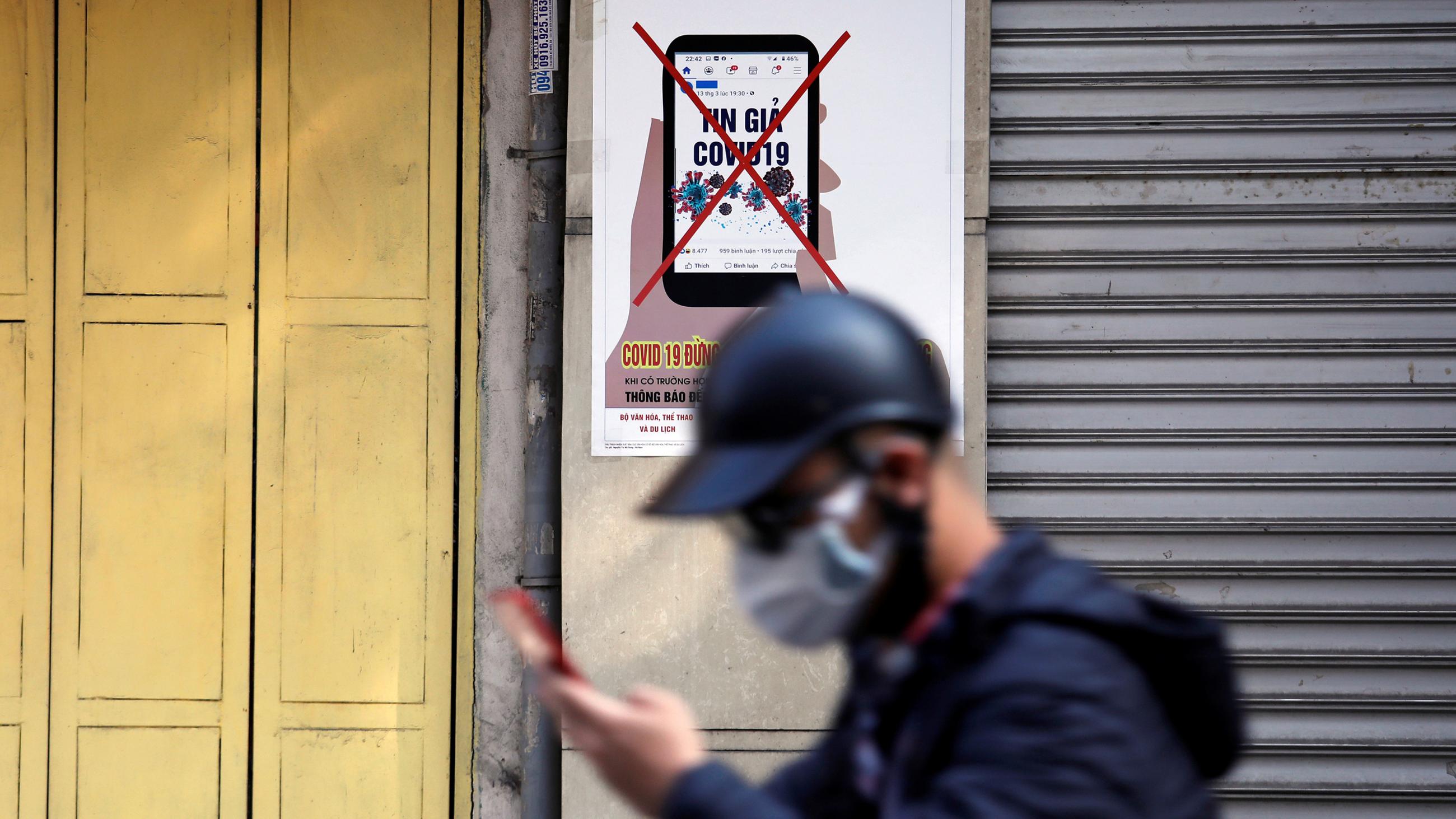 Picture shows a man with a hat walking out of focus in the foreground against a PSA picture posted on a wall. 