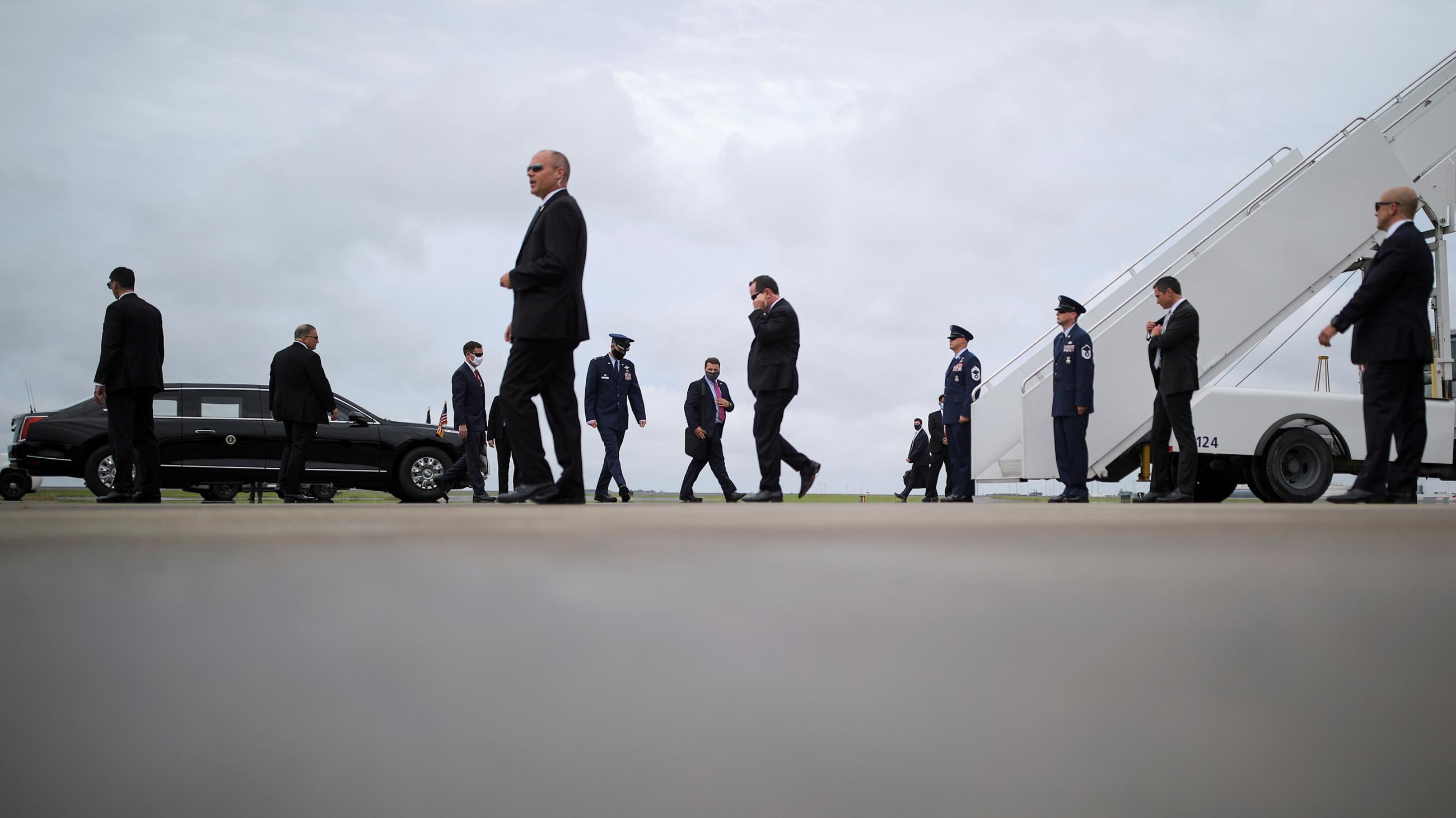 The photo shows a plane on the tarmac as well as a limosine from a distance with lots of people in suits walking about. 