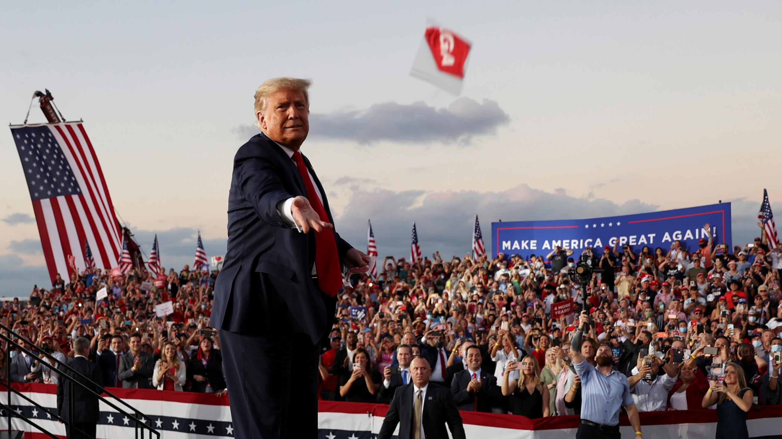 The photo shows the president tossing a mask that appears to have "MAGA" written on it against a backdrop of a large crowd of cheering people, many of whom can be seen not wearing masks. 