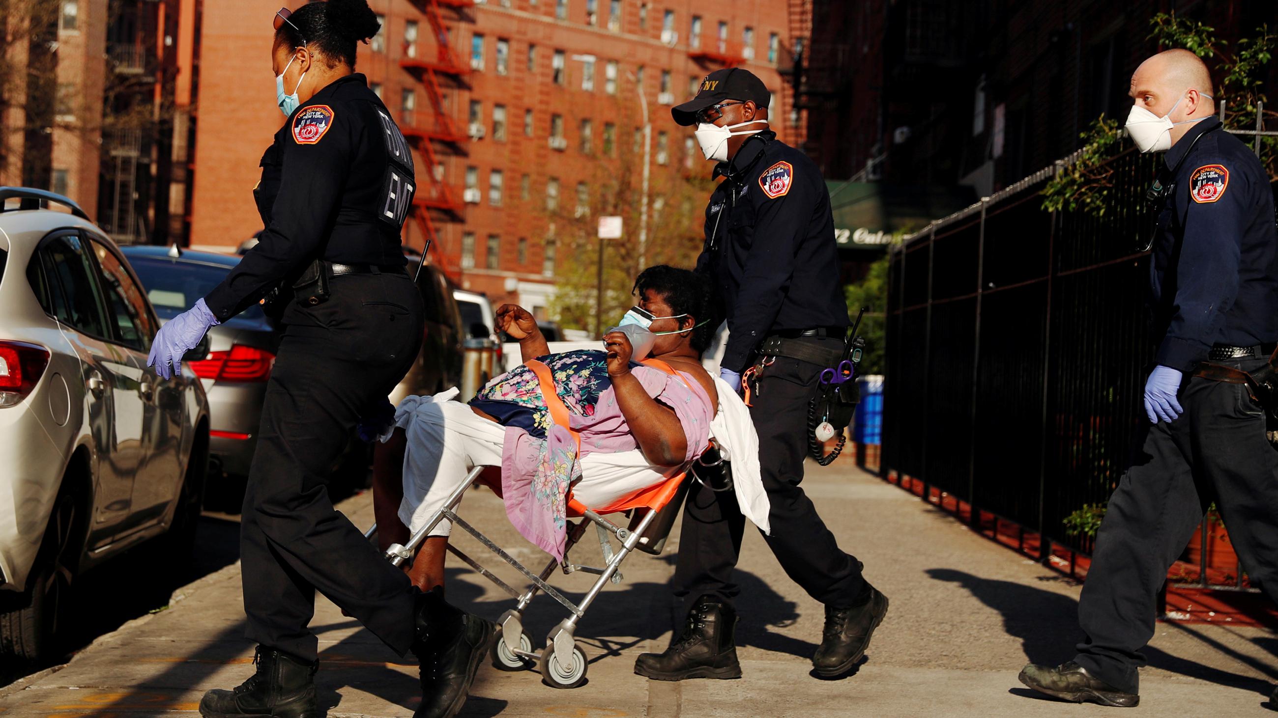 The photo shows three EMTs wheeling a gurney with a woman on a clear day in some part of the city. 