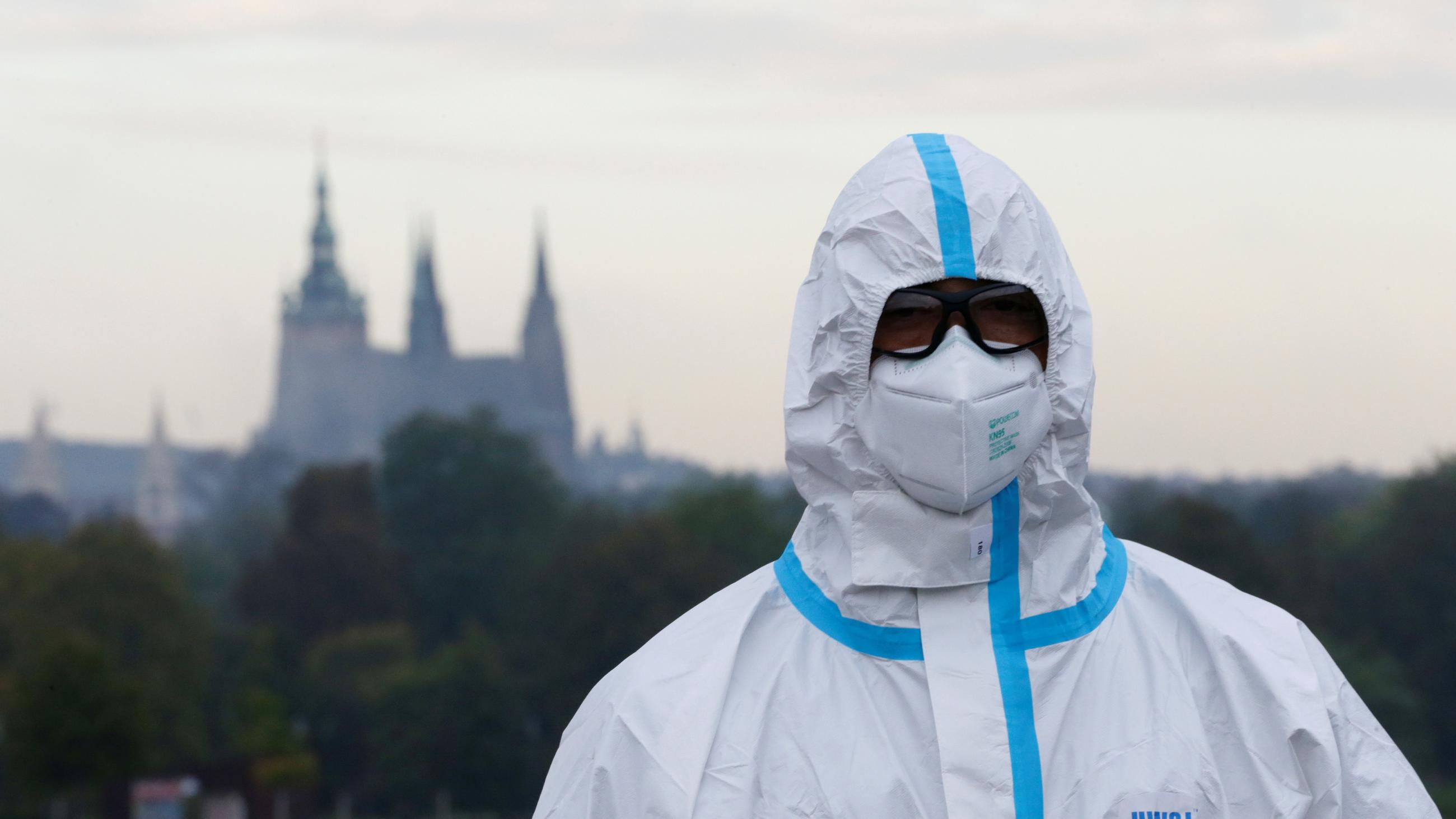 An election committee member wearing full PPE looks on while waiting for voters at a a drive-in polling station ahead of the country's regional election in Prague, Czech Republic. A castle can be seen in the background.