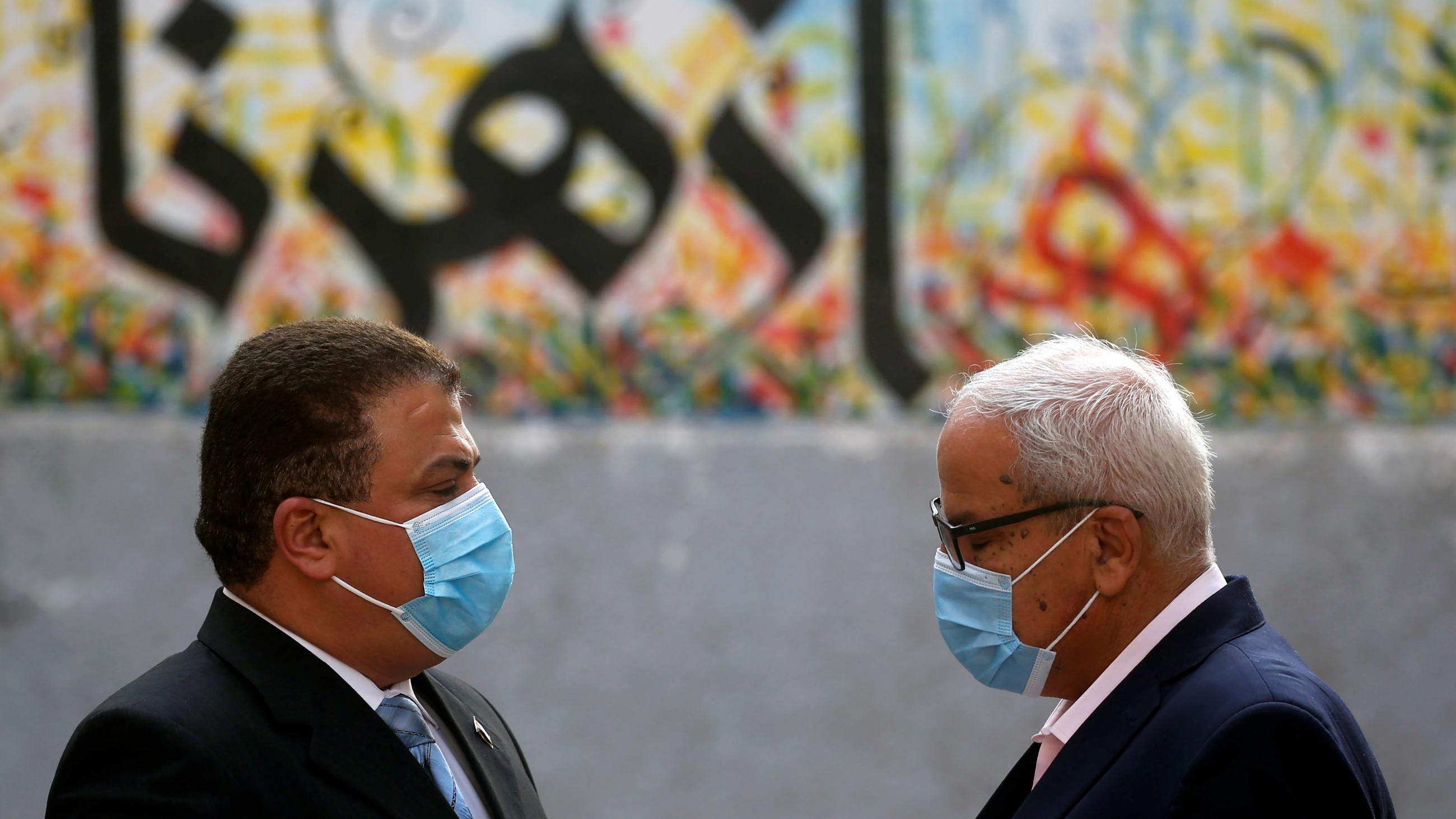 Men wearing face masks stand in front of a mural with Arabic writing and wait to cast their votes outside a polling station during Egypt's parliamentary election in Cairo, Egypt, on November 7, 2020.