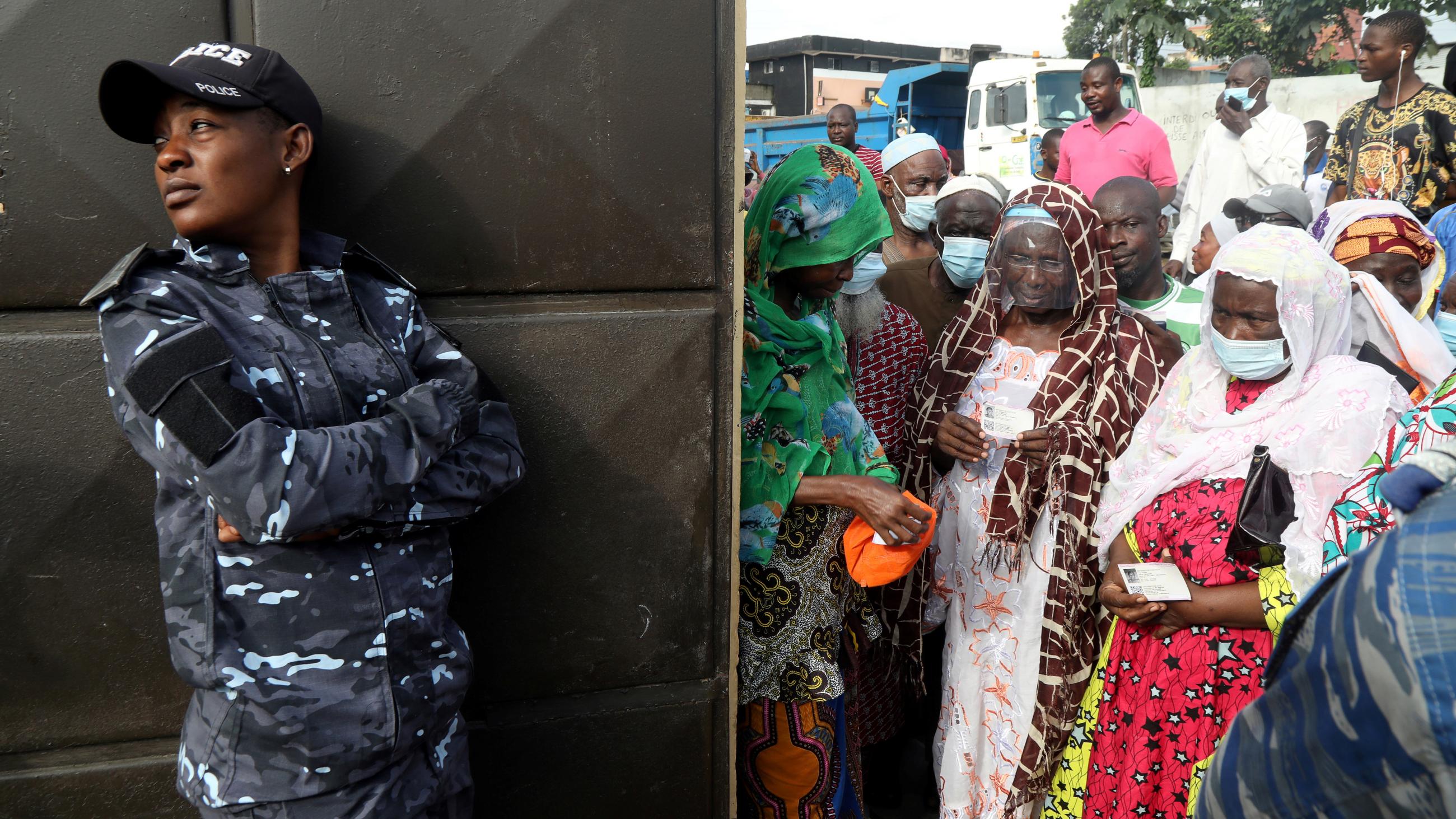 A soldier stands by a wall and looks away from people waiting to cast their votes during the presidential election in Abidjan, Ivory Coast on October 31, 2020. 