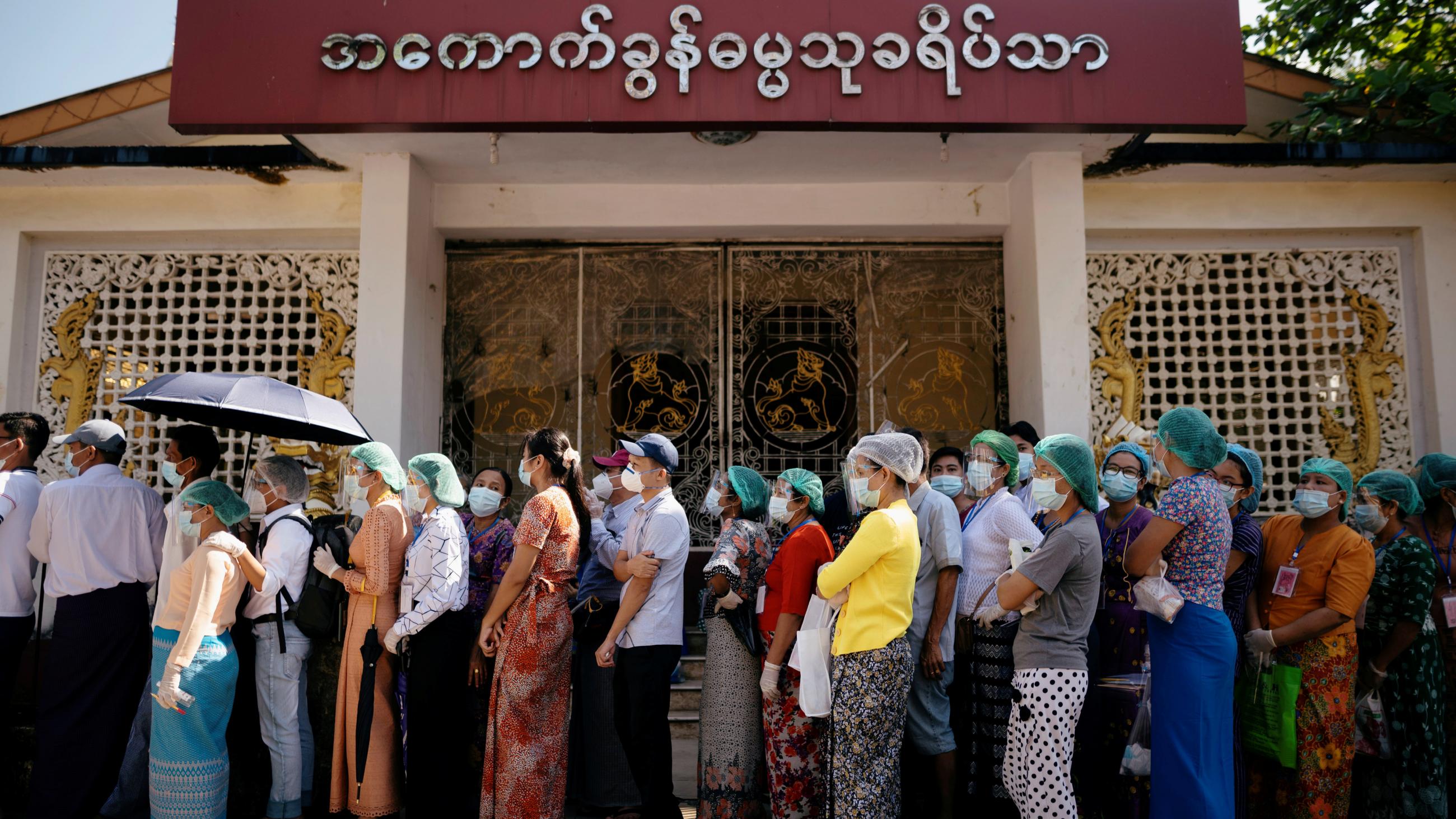 People wearing protective masks stand in line, closely together, waiting to cast their ballots for the general election at a polling station in Yangon, Myanmar on November 8, 2020.